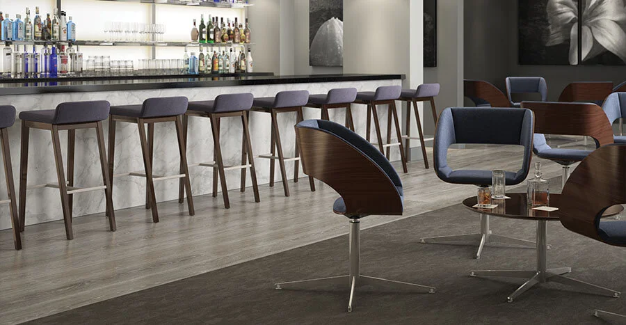 Modern bar area with a marble countertop, bar stools, comfortable armchairs, and a small table with drinks in a lounge or hotel setting.