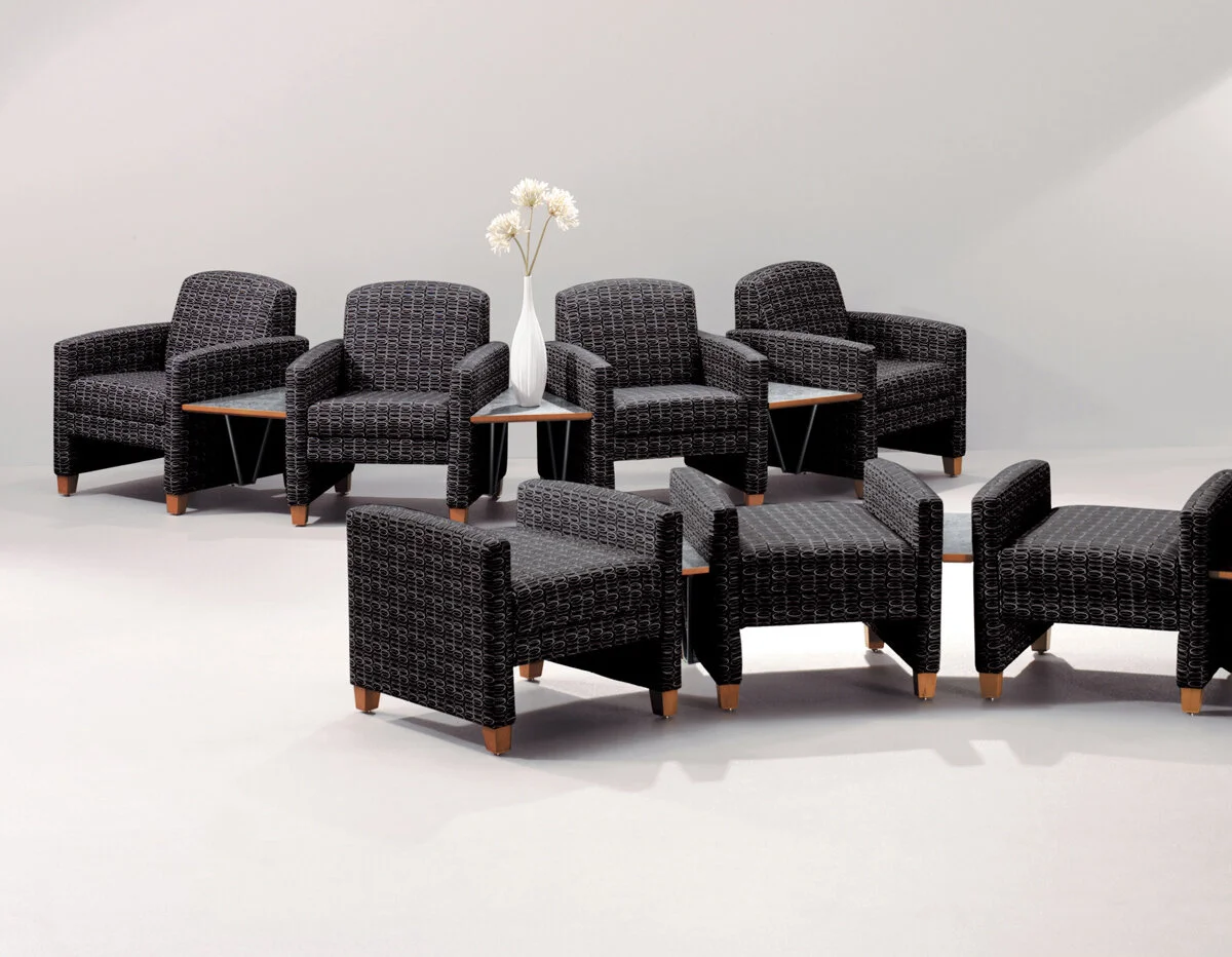 Eight black woven armchairs arranged in two groups with a small table in between, holding a white vase with white flowers, against a plain white background.