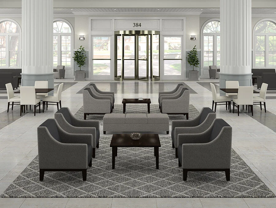Modern hotel lobby with gray armchairs and sofas arranged in a circle, black coffee tables, white accent chairs with tables, large windows, tall white columns, planters with green plants, and a revolving door at the entrance.