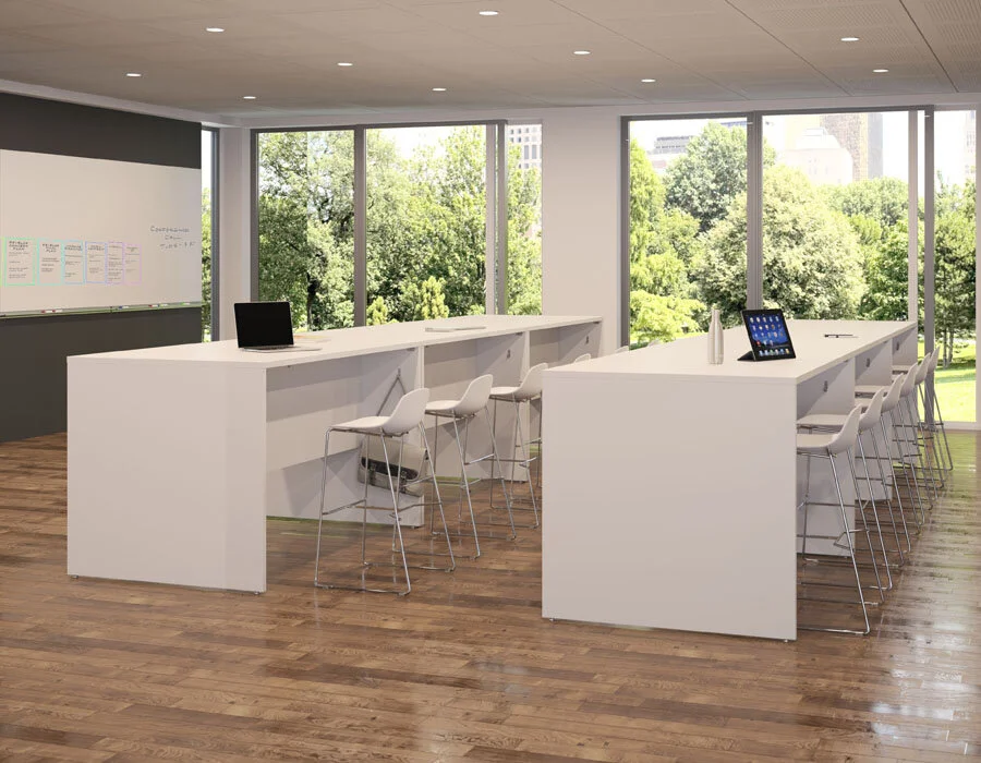 Modern office space with white high-top tables, white chairs, laptops, and tablets, large windows overlooking a green park.