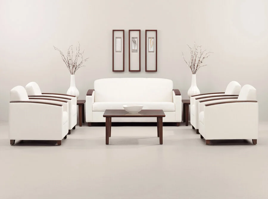 Minimalist white living room with a sofa, four matching armchairs, a coffee table, tall vases with dry branches, and three framed pictures on the wall.