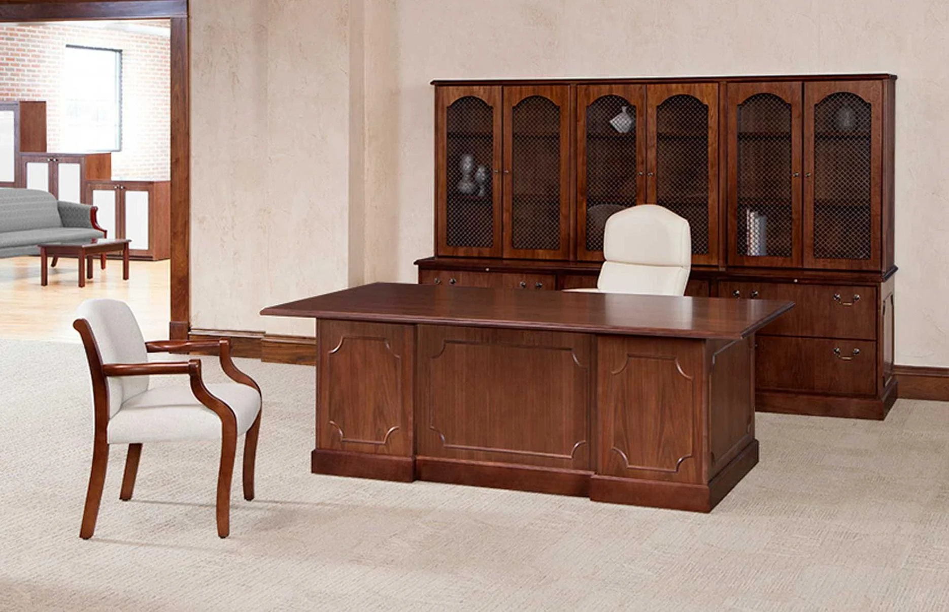 An office with a wooden desk, a white leather office chair, a wooden cabinet with glass doors, and an upholstered white chair with wooden armrests.