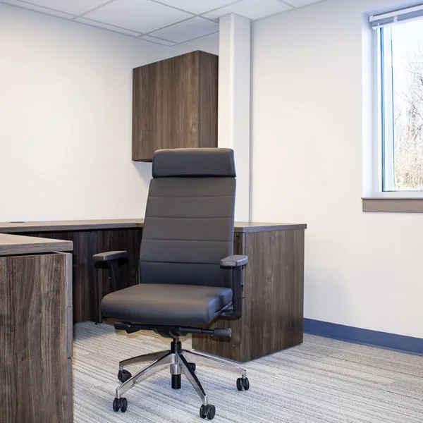 Empty black high-back office chair in a minimalistic office with wood furniture and a window.