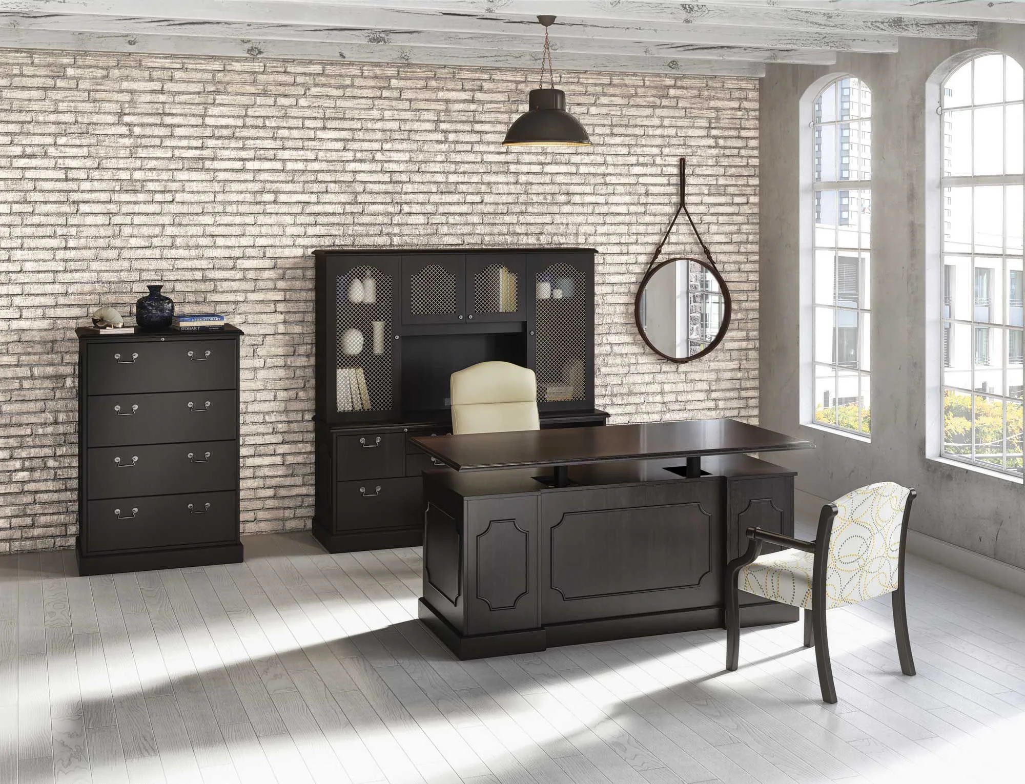 An office with a brick accent wall and large windows. There is a black desk with a cream-colored chair, a black filing cabinet, a bookshelf with glass doors, a round mirror, and a black pendant light.