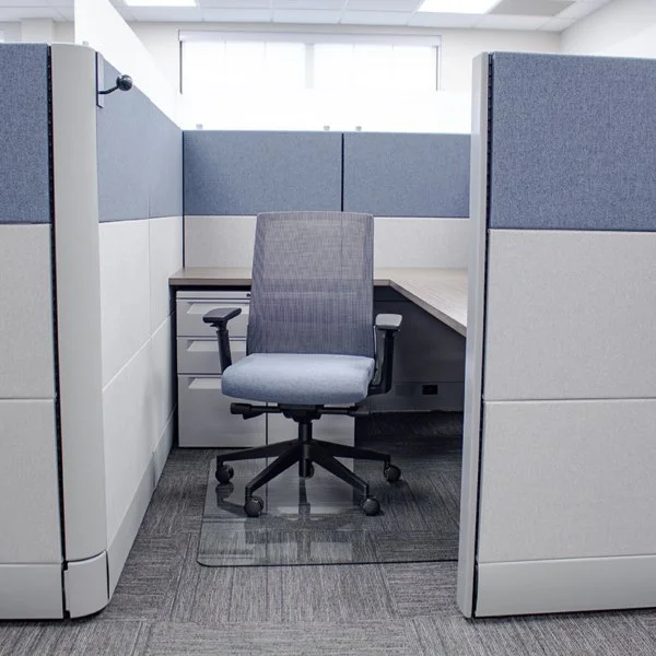Empty office cubicle with gray walls, a gray office chair, and a L-shaped desk in an office setting.