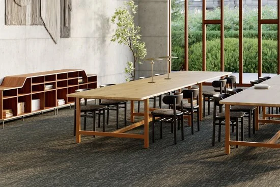 Modern office conference room with large wooden table, black chairs, built-in bookshelf, and large window overlooking greenery.