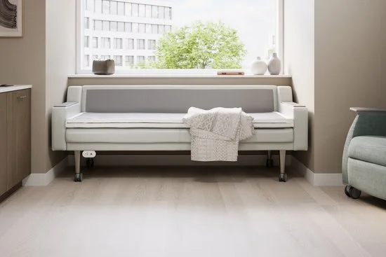 White living room with a minimalist couch, decorative items on the windowsill, and a large window showing a building and trees outside.