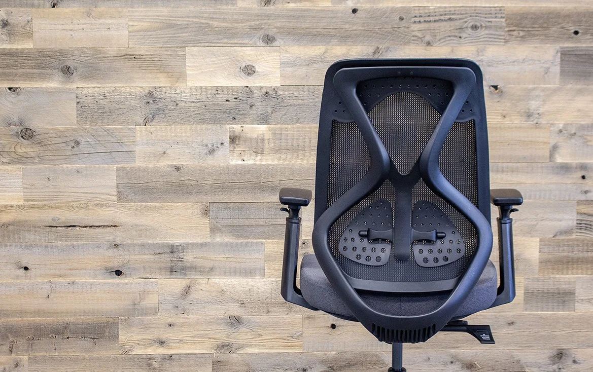 An ergonomic office chair with a black backrest and armrests, positioned on a light wooden floor.