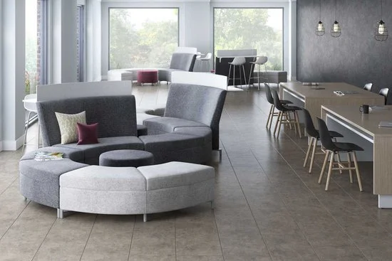 Modern lounge and dining area with large windows, circular sectional sofa with pillows, and a long dining table with chairs.