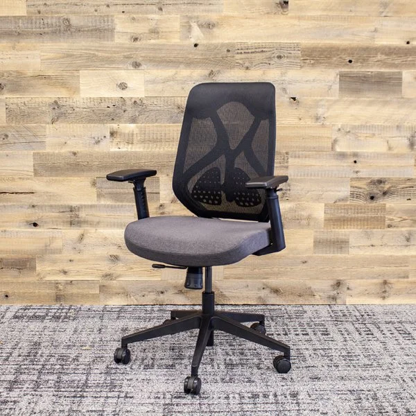 A black and gray office chair with armrests on a gray and black patterned carpet in front of a light wooden wall.