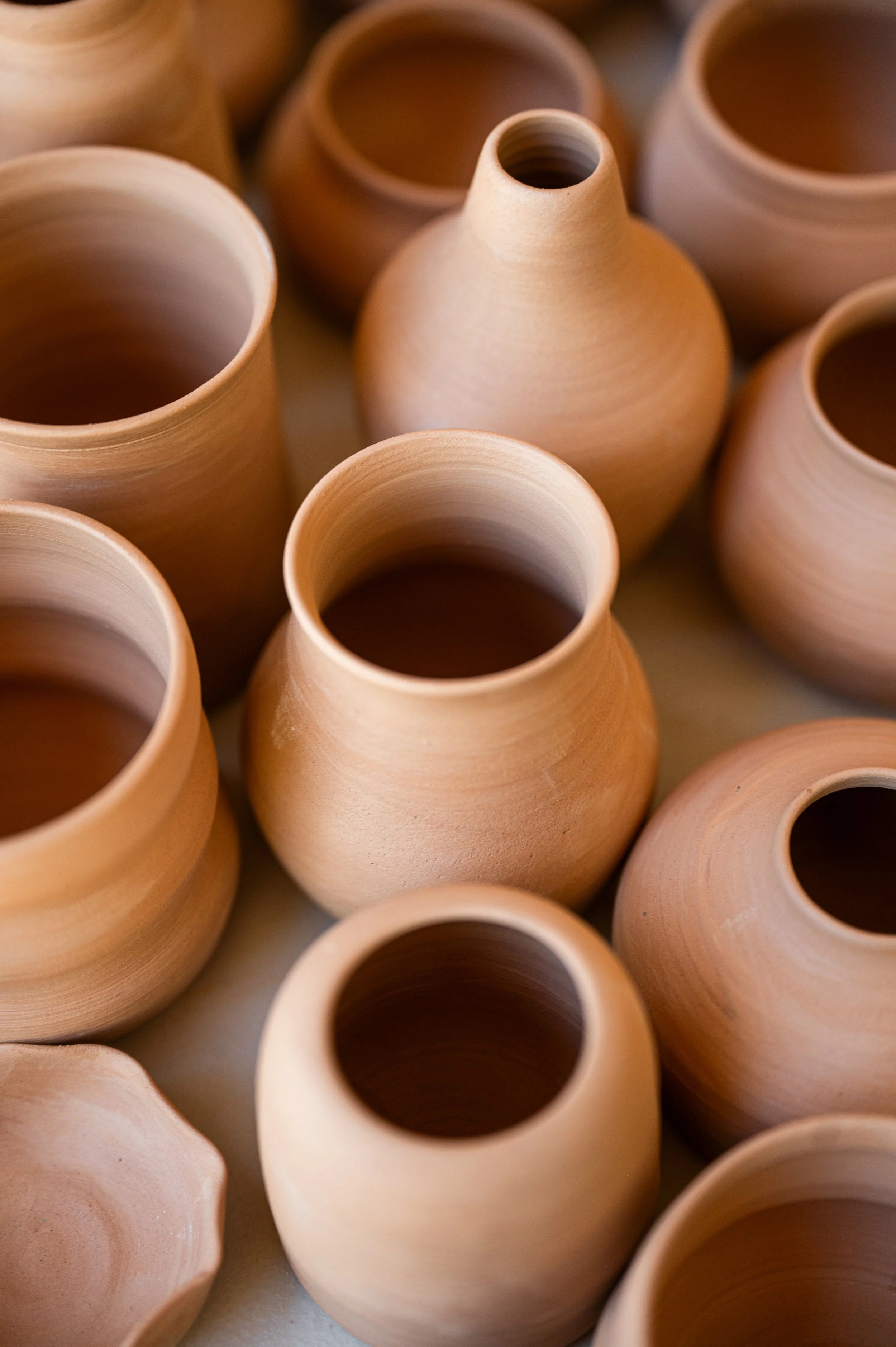 Multiple unglazed clay pots with narrow necks, arranged closely together.