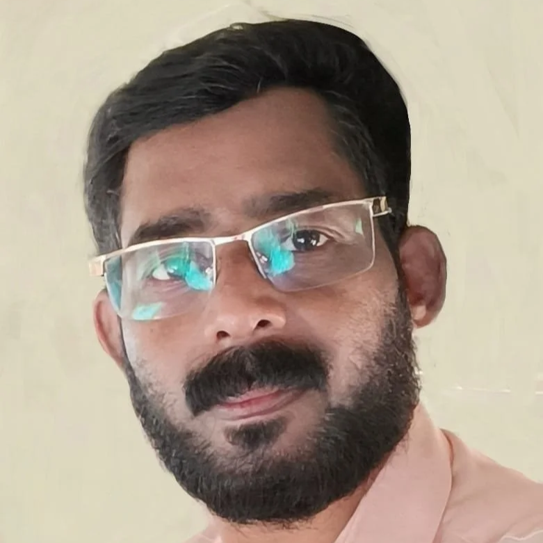 Close-up of a man with glasses, dark hair, and a beard, looking at the camera against a light background.