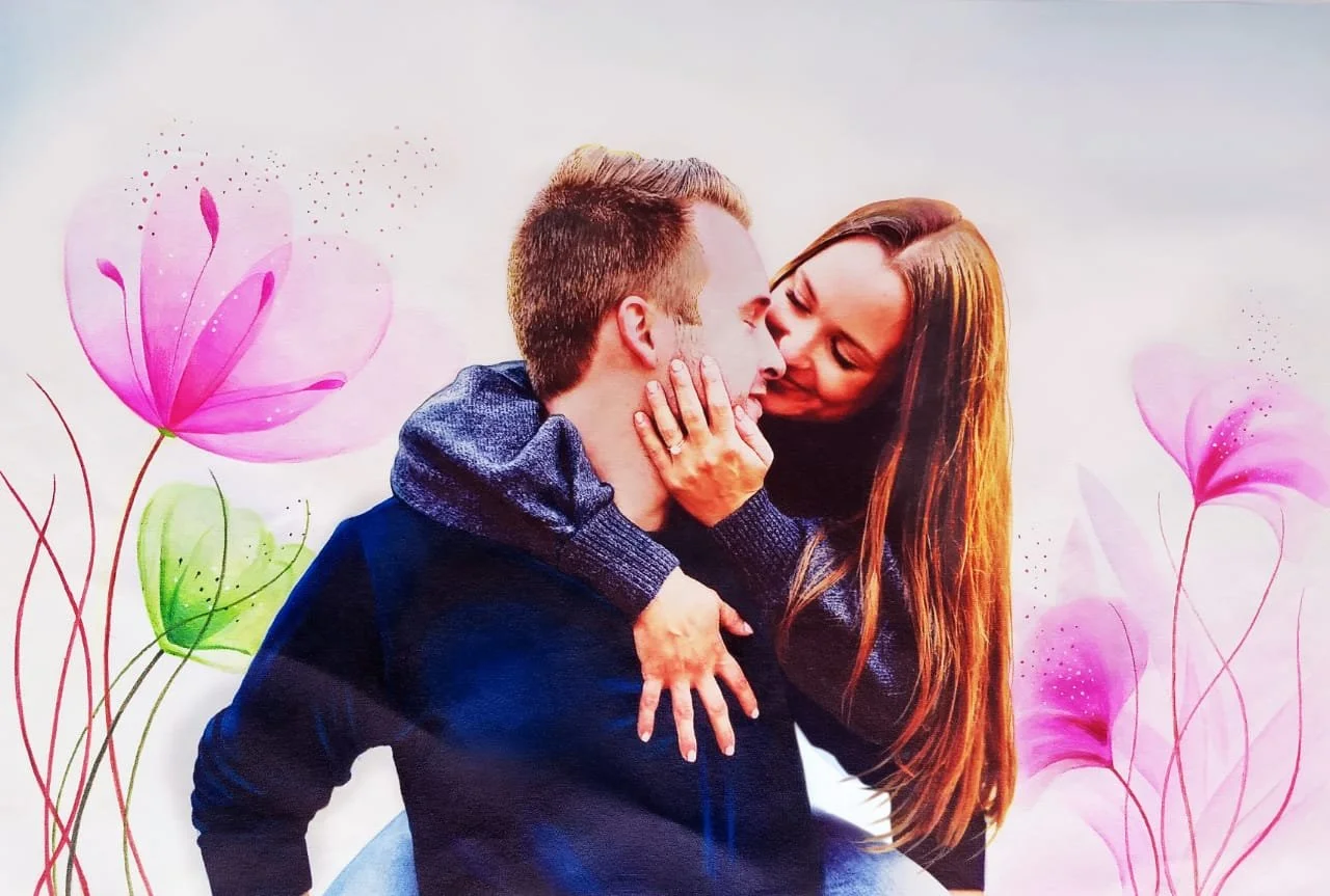 A man and woman share an intimate moment, with the woman gently holding the man's face as they lean close, surrounded by pink and purple floral illustrations.