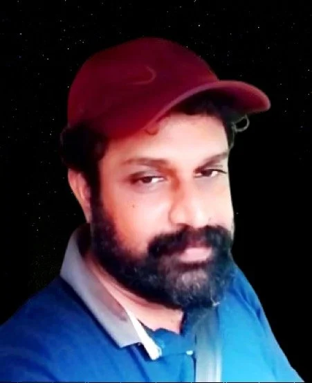 A man with a beard wearing a red cap and a blue shirt against a starry background.