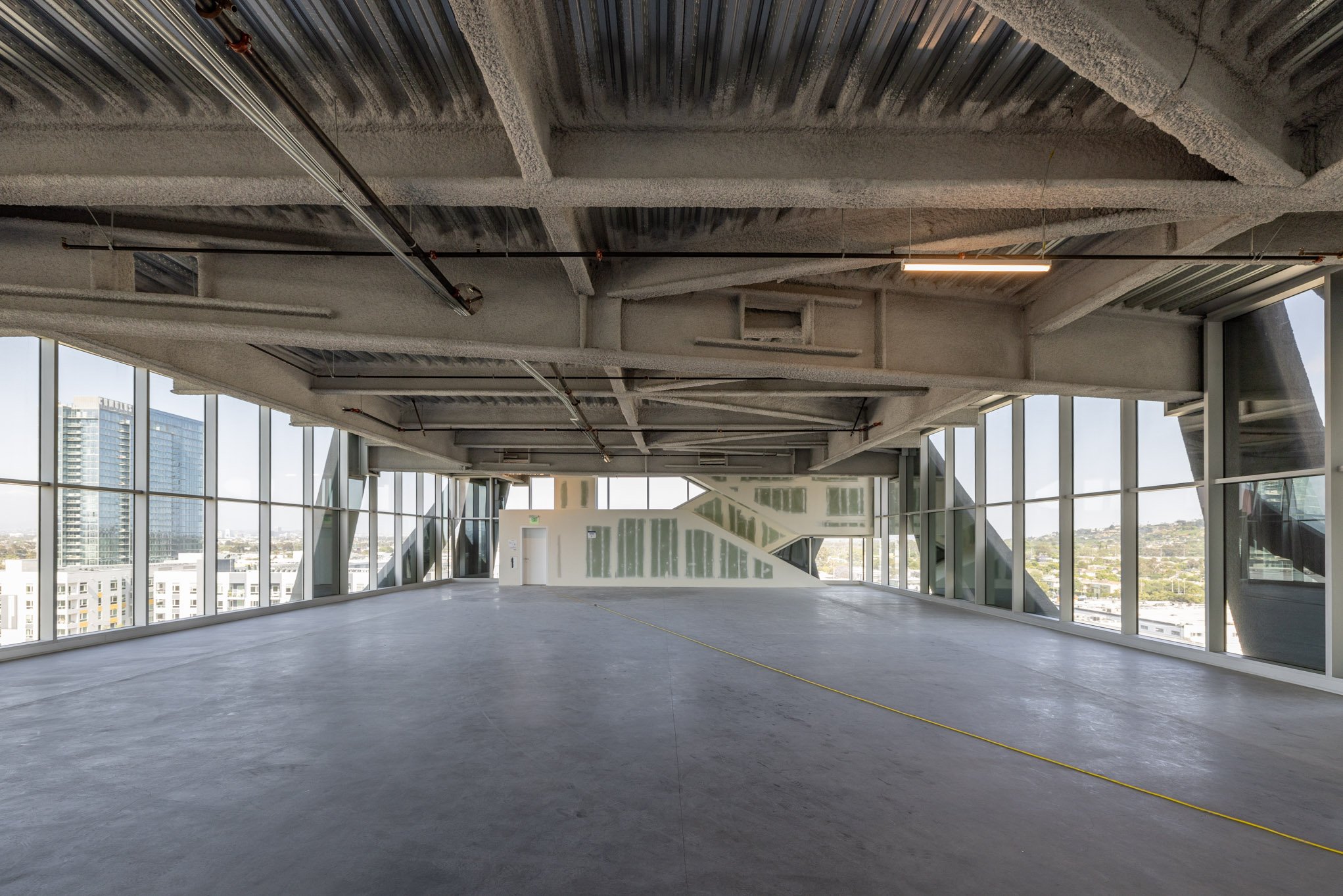 Empty modern office space with large windows, exposed ceiling, and a polished concrete floor.