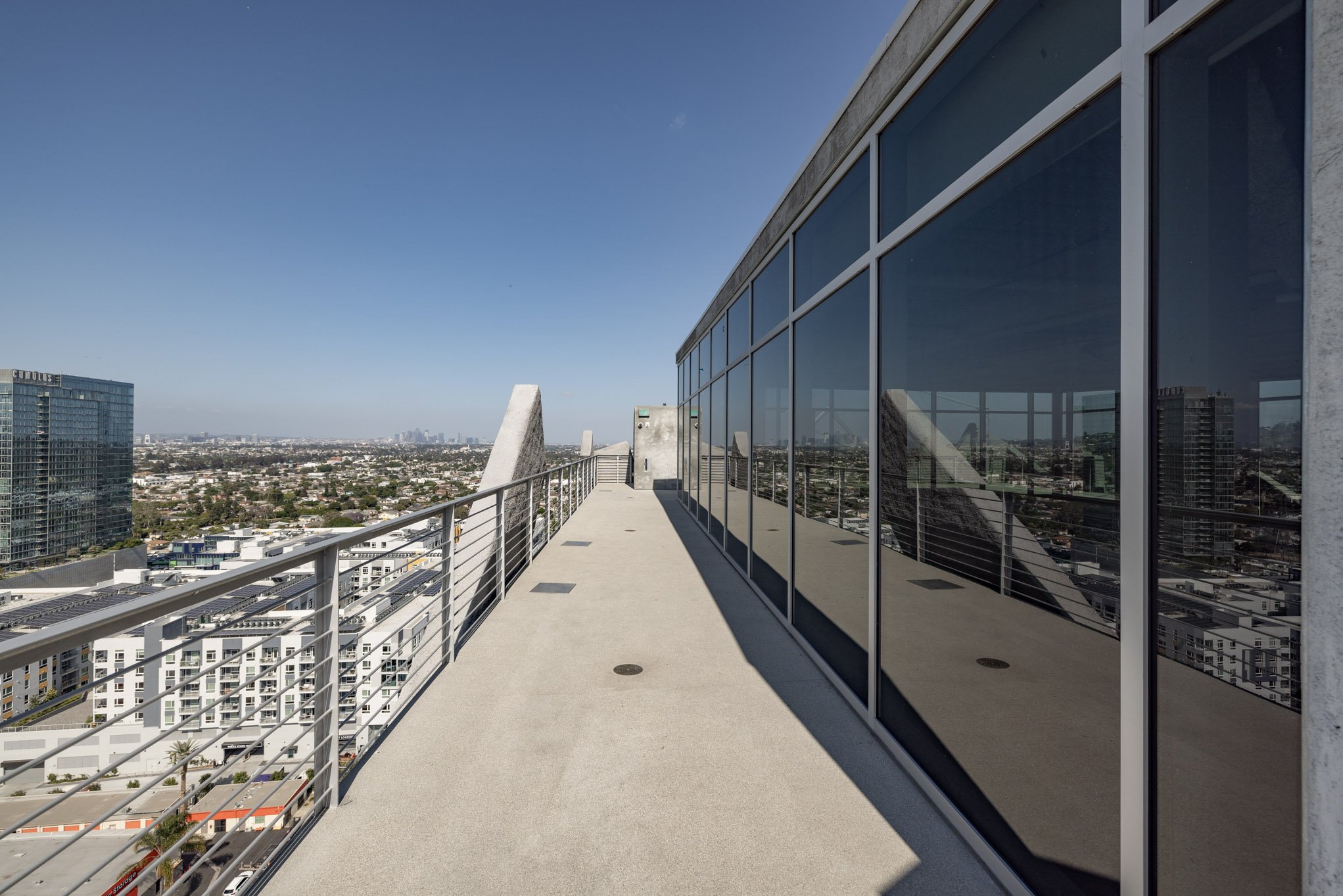 Rooftop terrace with glass-walled section and city skyline view under clear blue sky.
