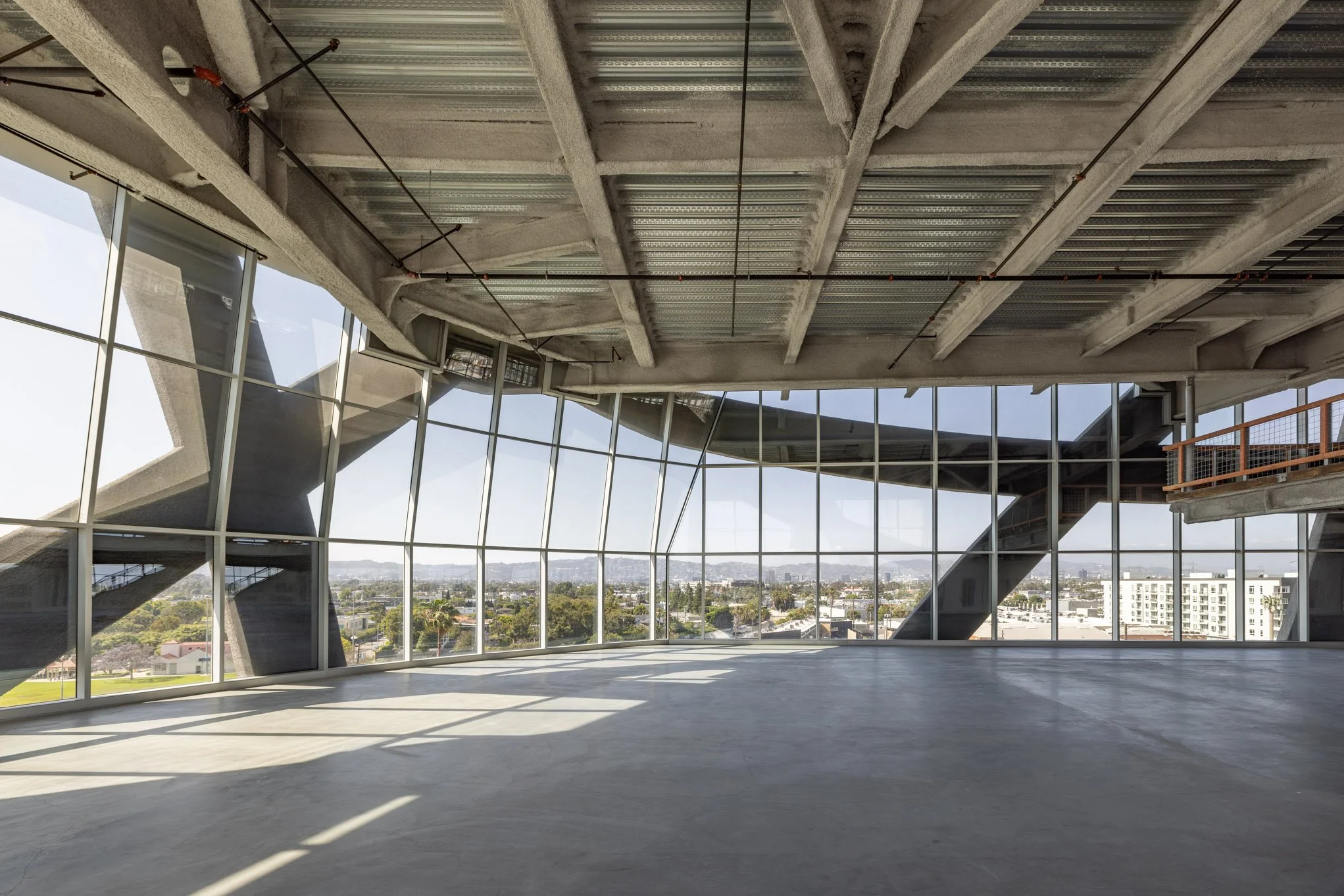 Empty modern interior space with large glass windows and unfinished ceiling, overlooking a cityscape.