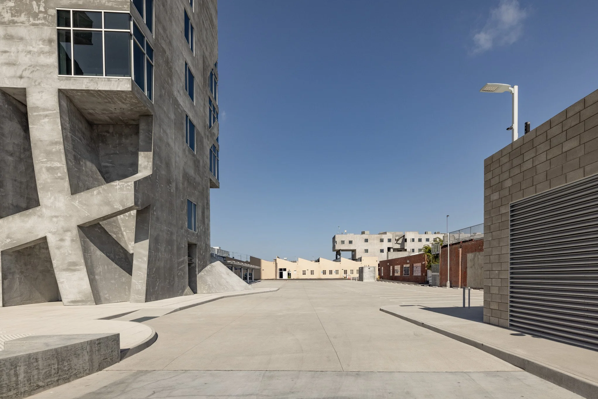 Empty urban street with modern buildings, clear blue sky, and minimal shadows.