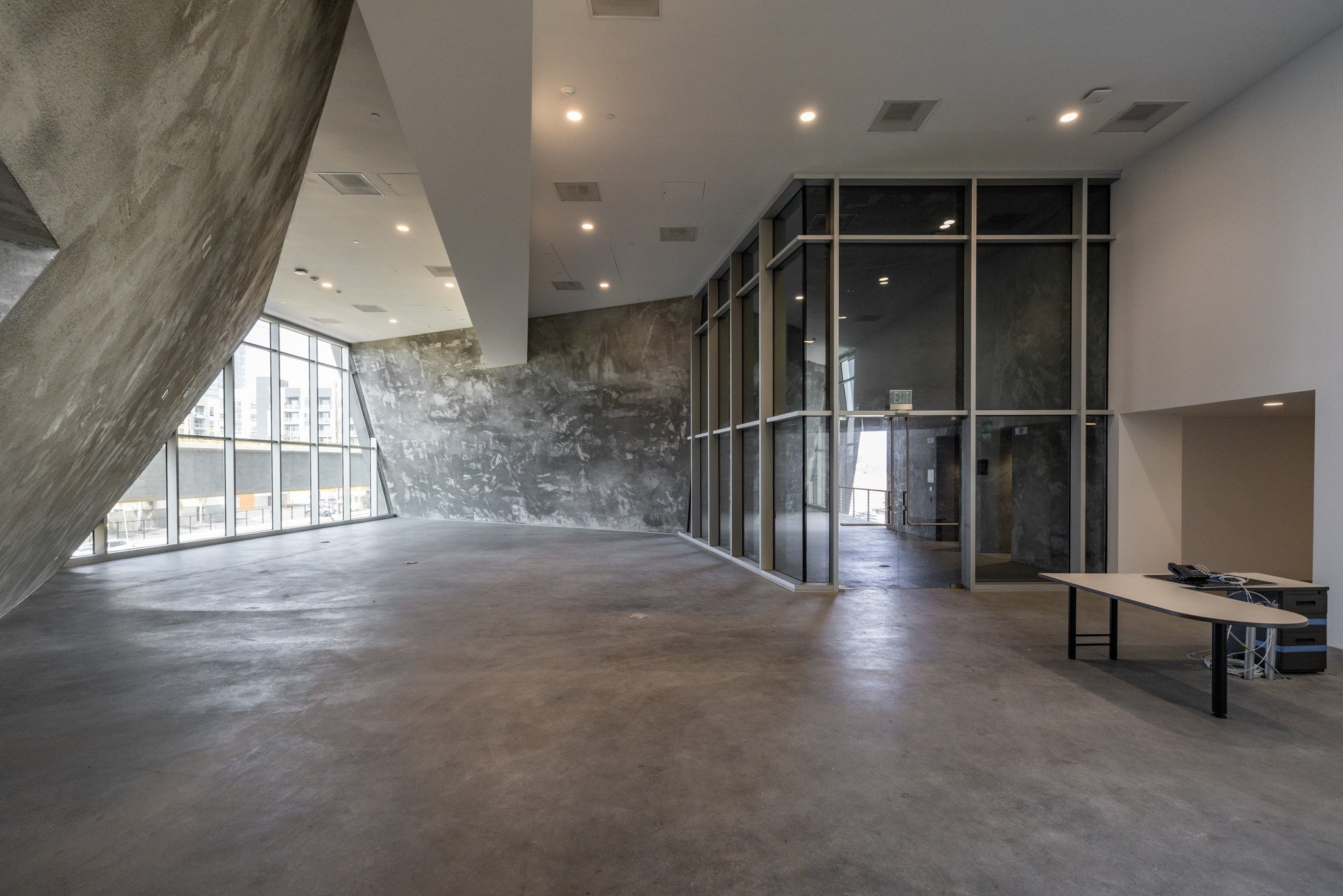 Empty modern office space with concrete floors, large windows, and glass partition walls.