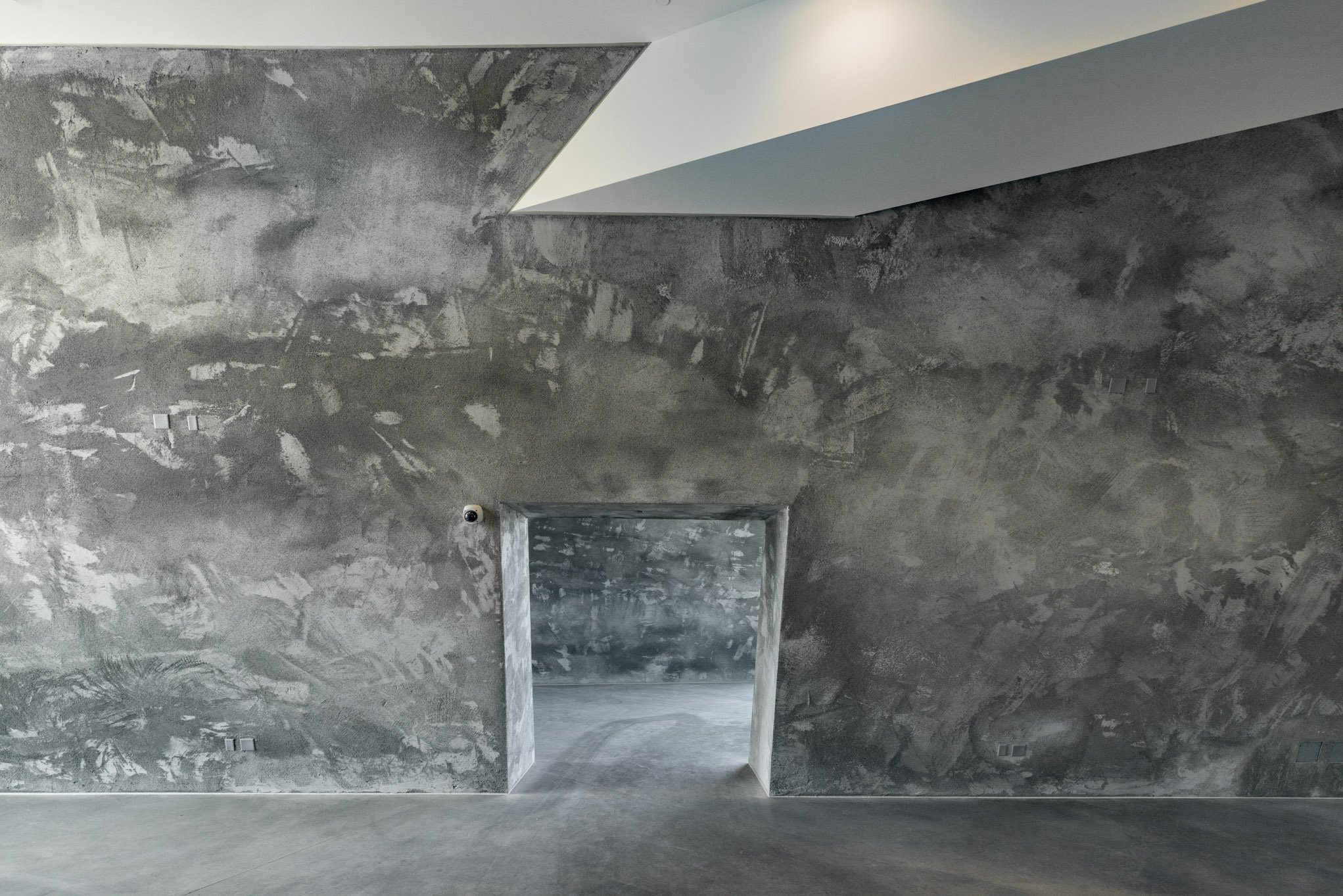 Interior view of a room with unfinished gray concrete walls and a doorway leading to another concrete space.