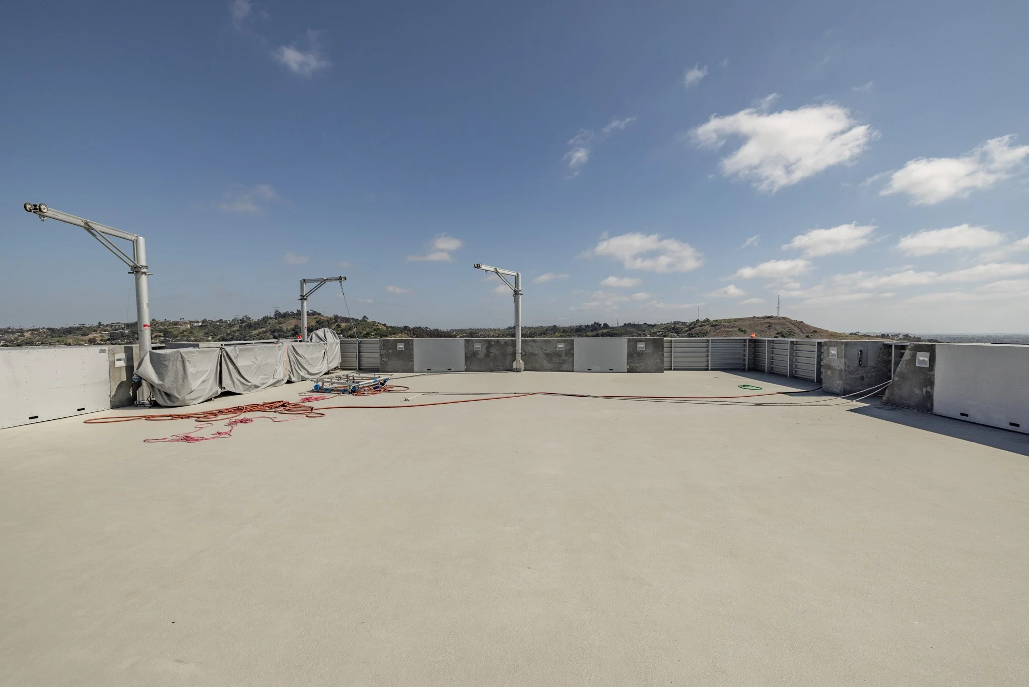 Empty rooftop with construction equipment, cables, and a view of distant hills under a partly cloudy sky.