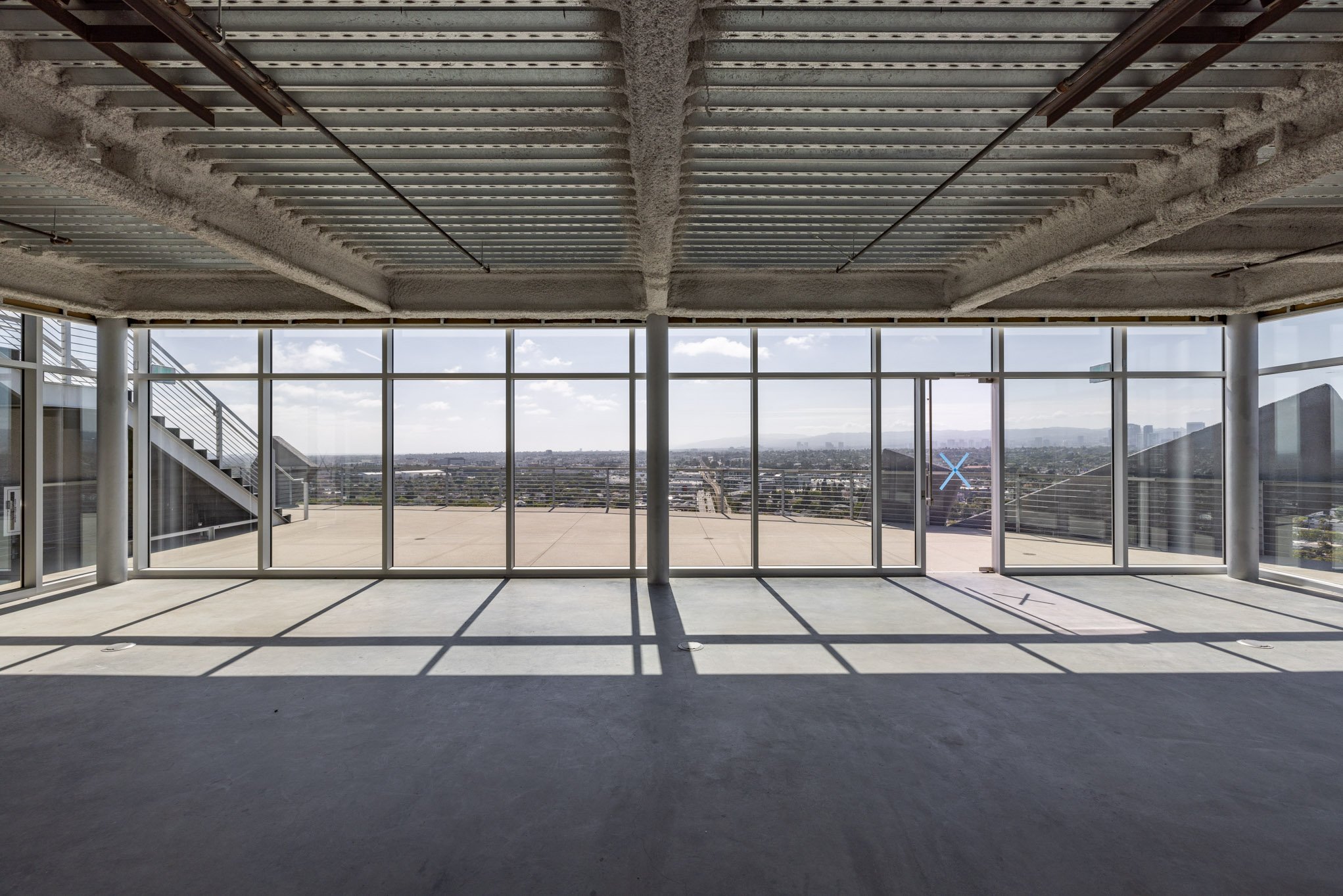 Empty room with large glass windows showing city skyline and blue sky with scattered clouds.