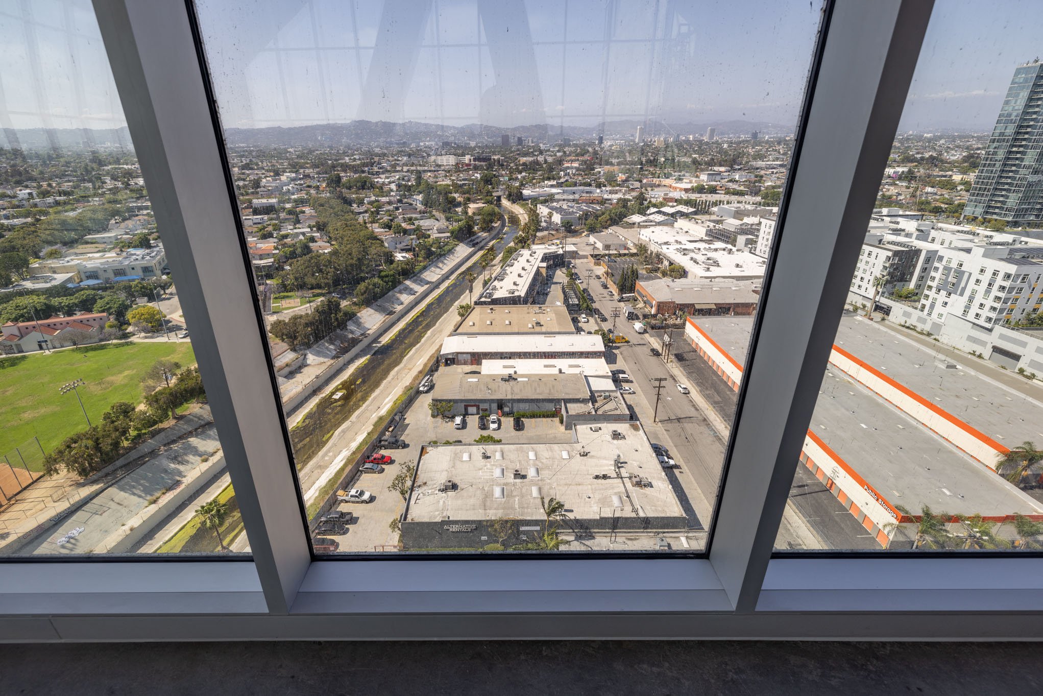 View of a cityscape through a window, showing buildings, streets, and a green park area.