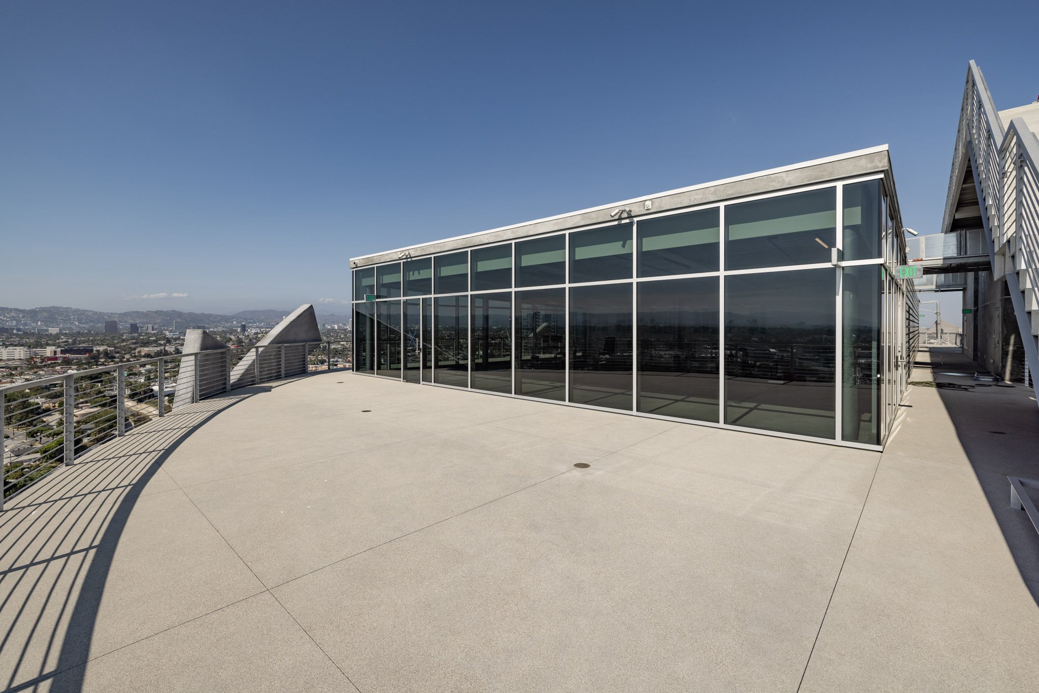 Empty rooftop terrace with glass-walled structure and city skyline in the background.