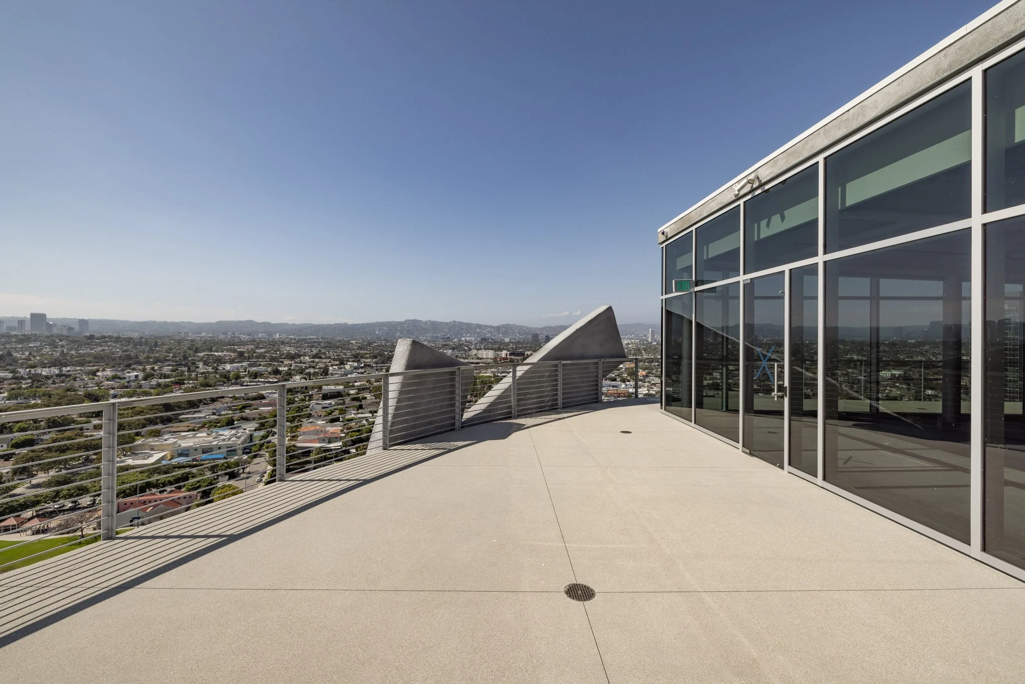 Rooftop terrace with glass walls, city skyline view, and decorative concrete sculptures.