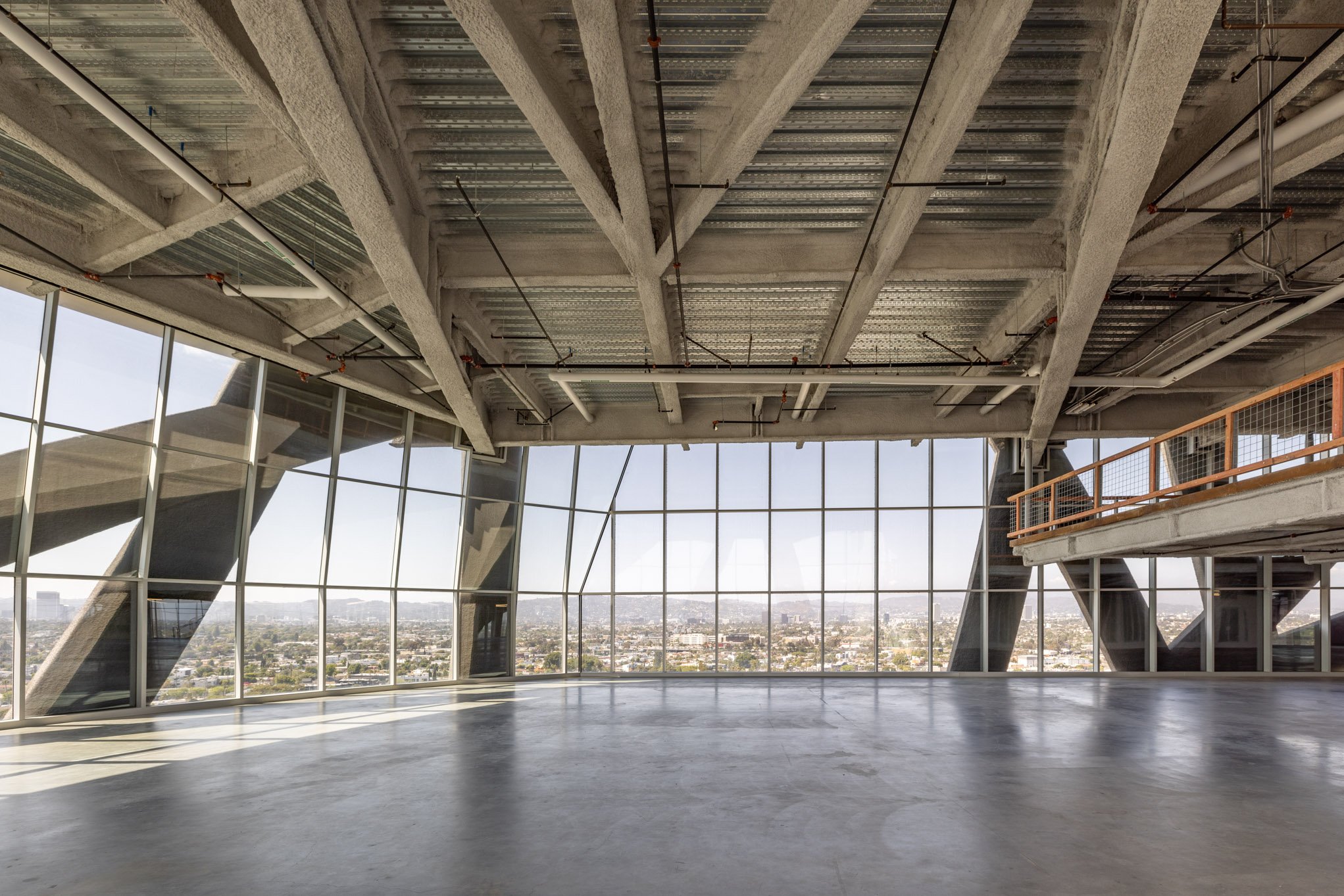 Empty interior of a modern building with large glass windows and an expansive view of a cityscape outside.