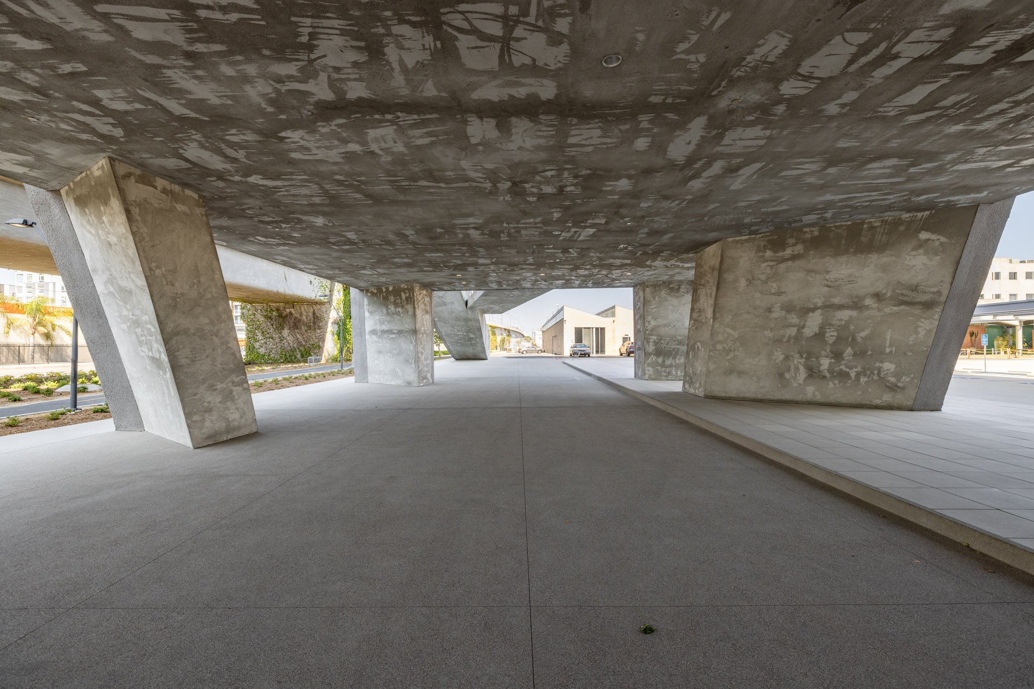 Underground parking area with concrete support columns and a paved sidewalk, modern architectural design.