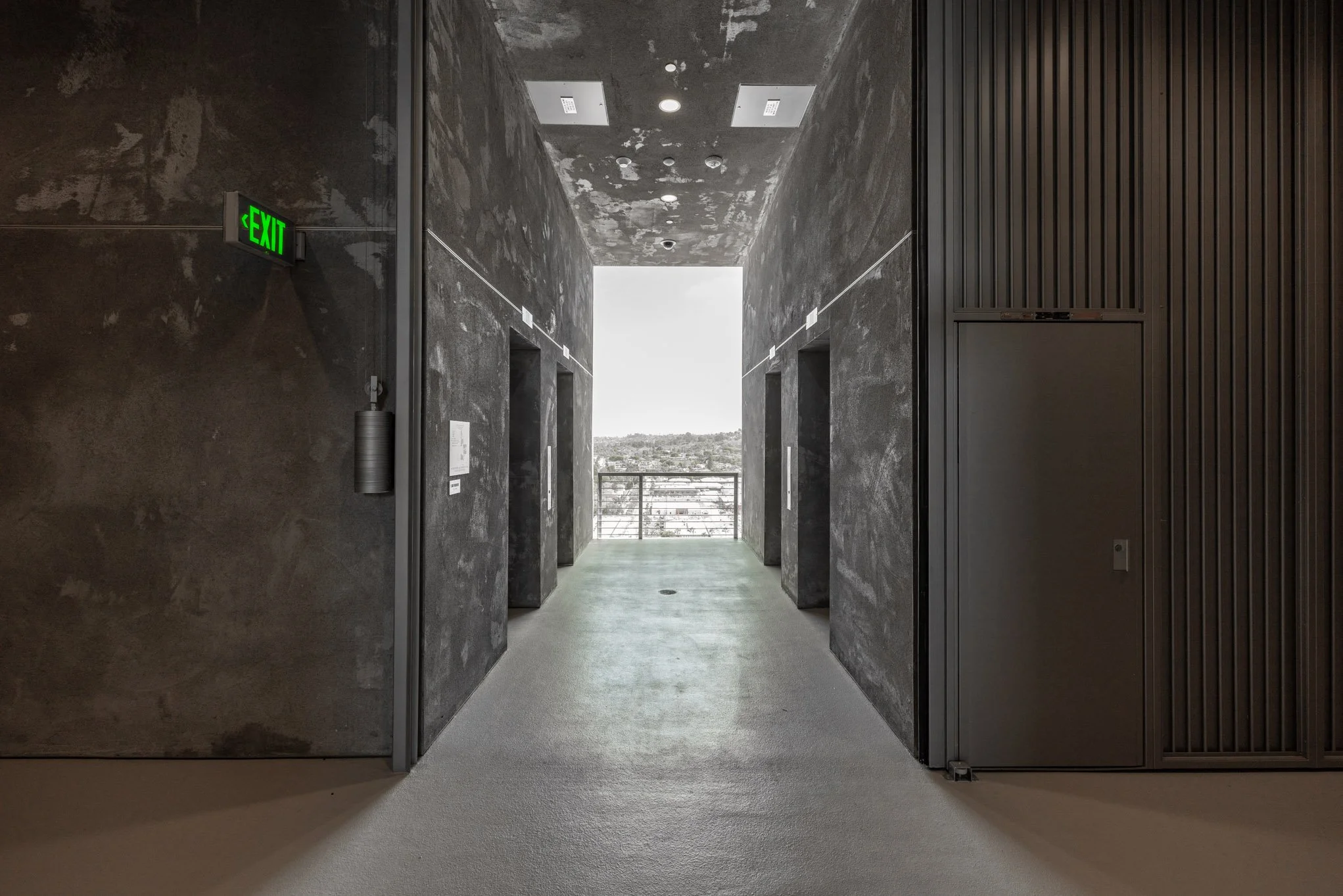 A hallway with four elevators and a view of a city skyline in the distance.