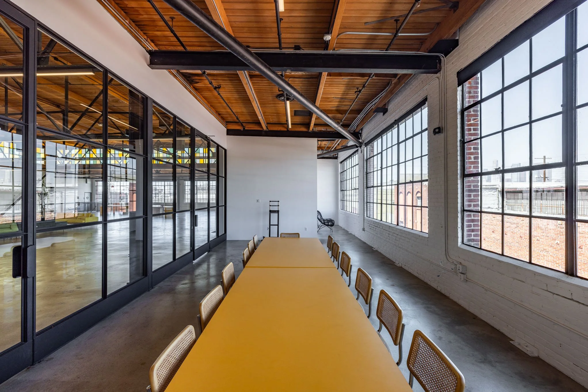 Modern conference room with large windows, yellow table, and wooden ceiling beams.