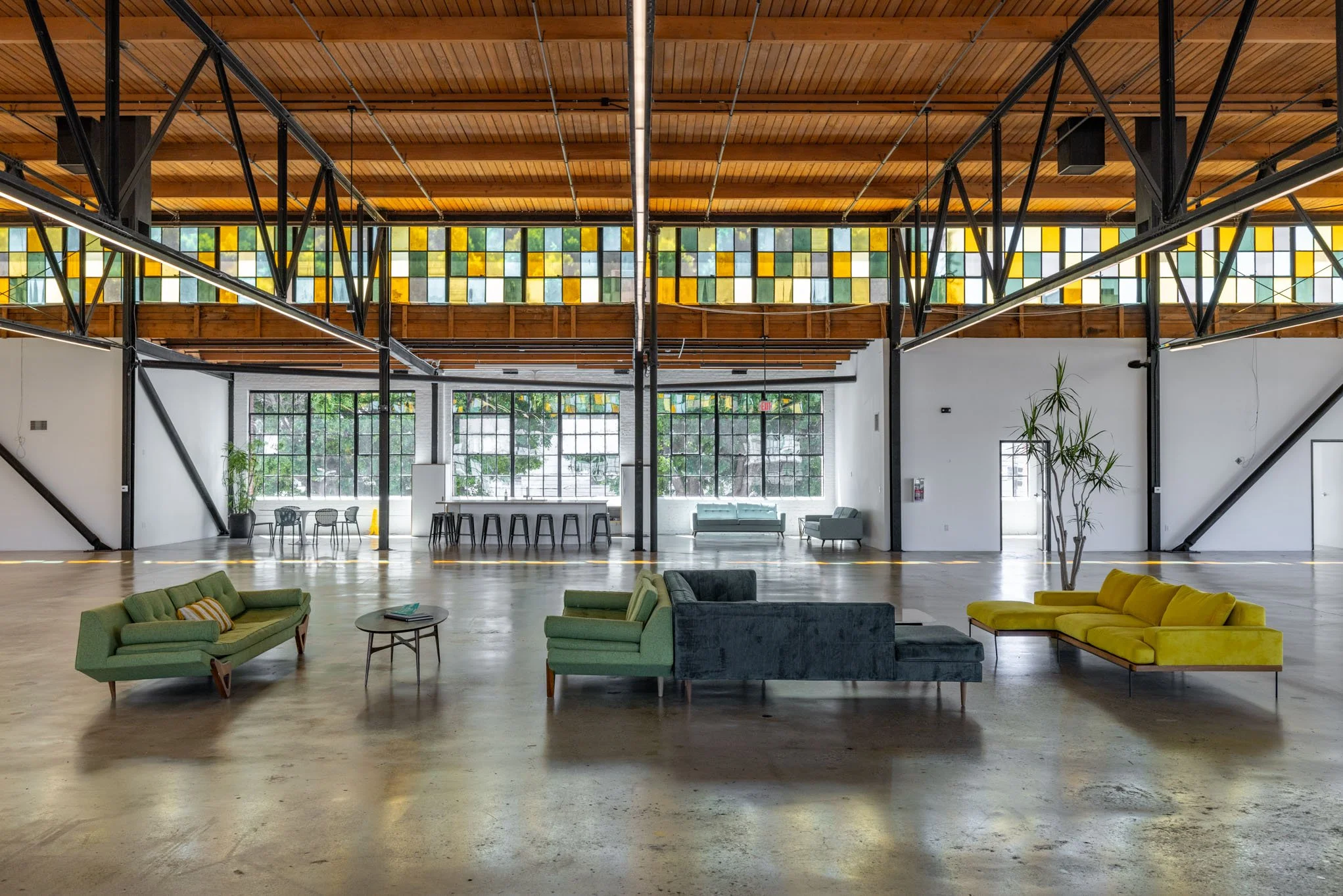 Spacious industrial-style lounge with colorful sofas, high ceilings, large windows, and modern decor.