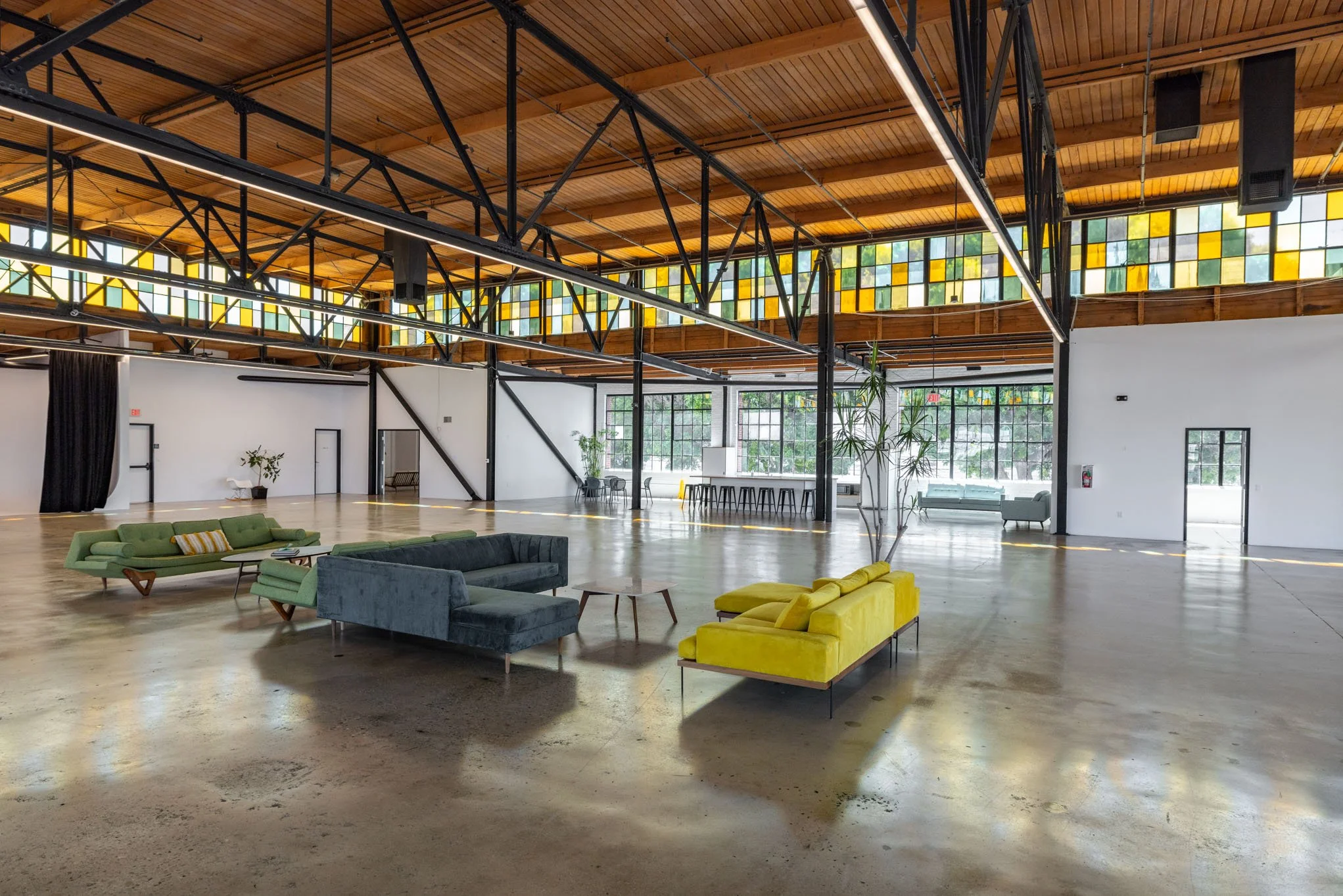 Spacious indoor lounge area with modern colorful sofas, wooden ceiling, and large stained glass windows letting in natural light.