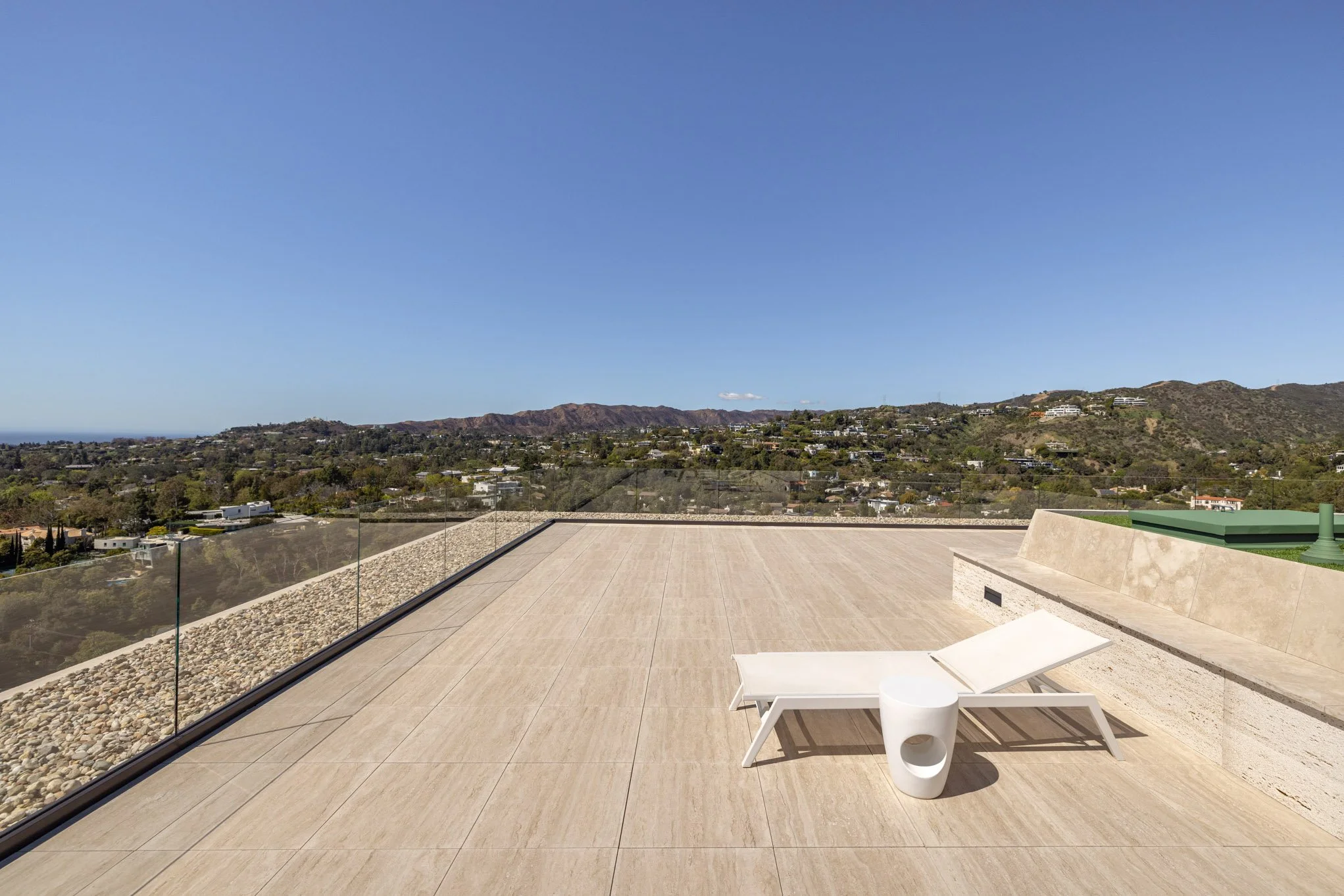 Luxury rooftop terrace with a white lounge chair and small side table overlooking a scenic view of distant hills and a clear blue sky.