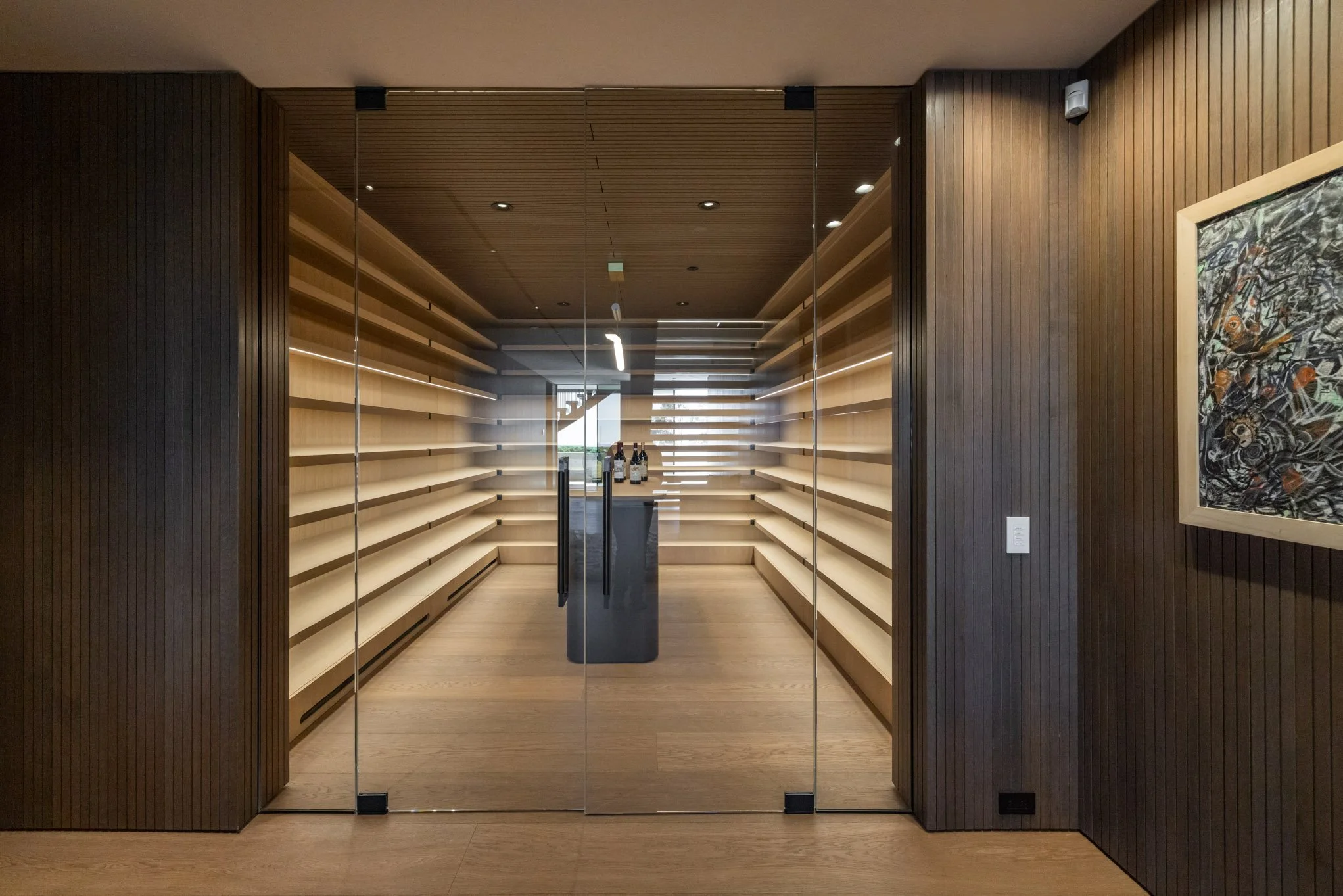 Empty wooden wine storage room with glass front door and bottles on display
