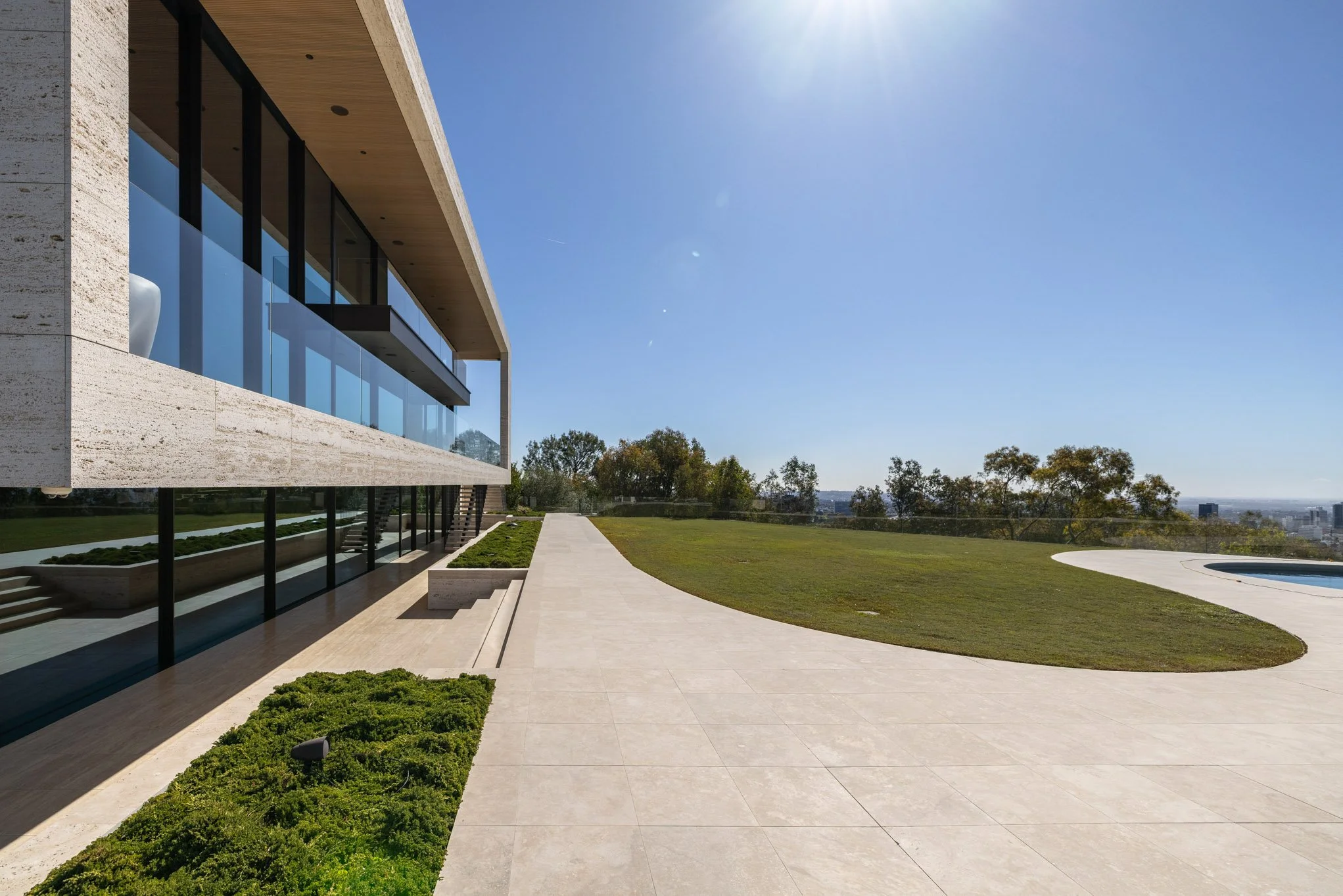 Modern house with large glass windows, a landscaped garden, and a swimming pool on a clear, sunny day.