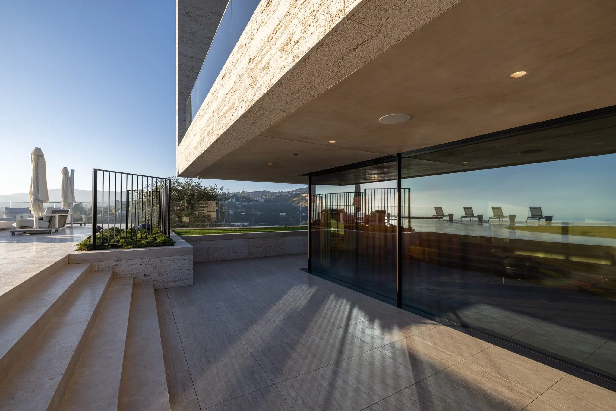 Modern outdoor terrace with lounge chairs, umbrellas, and glass walls on a sunny day.