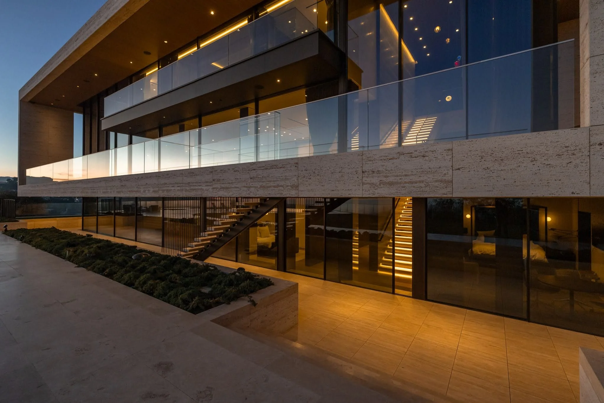 Modern multi-story building with illuminated glass staircases and balcony railings at dusk.