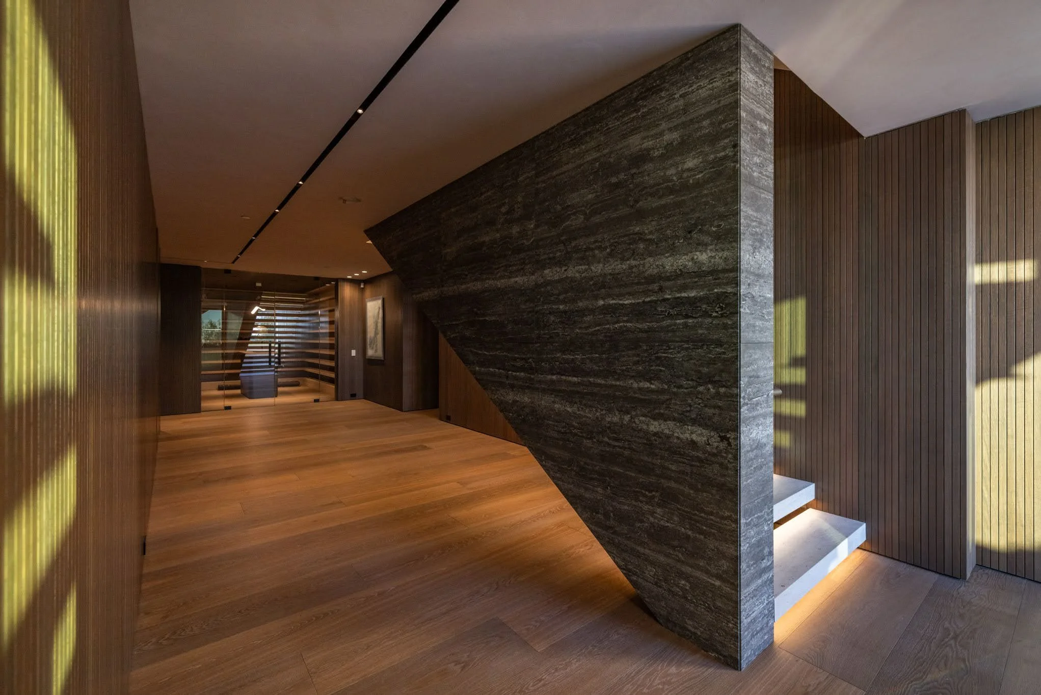 Modern interior with wood paneling, a dark stone wall, and a staircase partially visible through a glass door.