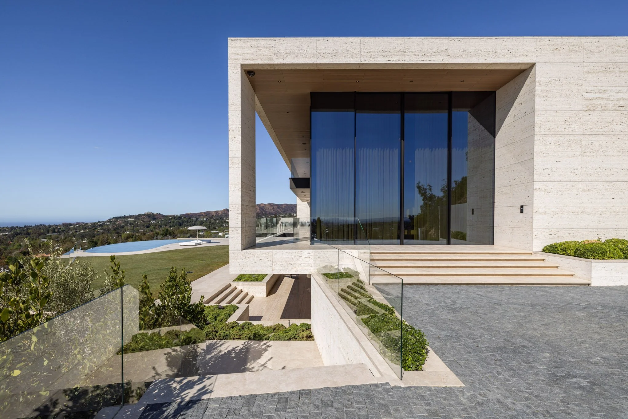 Modern house with large glass windows, outdoor stairs, and landscaped garden on a sunny day.