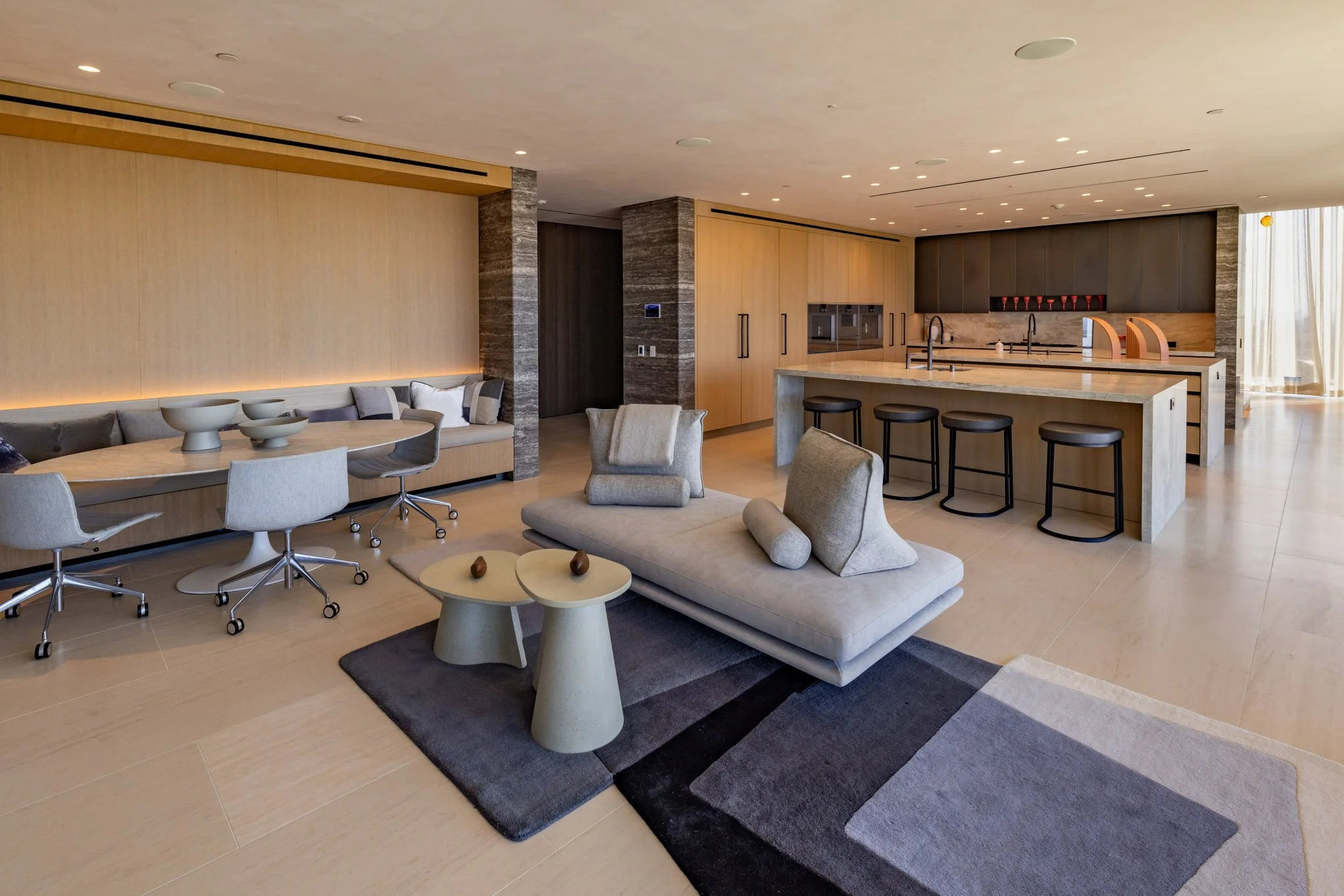 Modern open-concept living and kitchen area with neutral-colored furniture, a kitchen island with four barstools, and a dining table with chairs.
