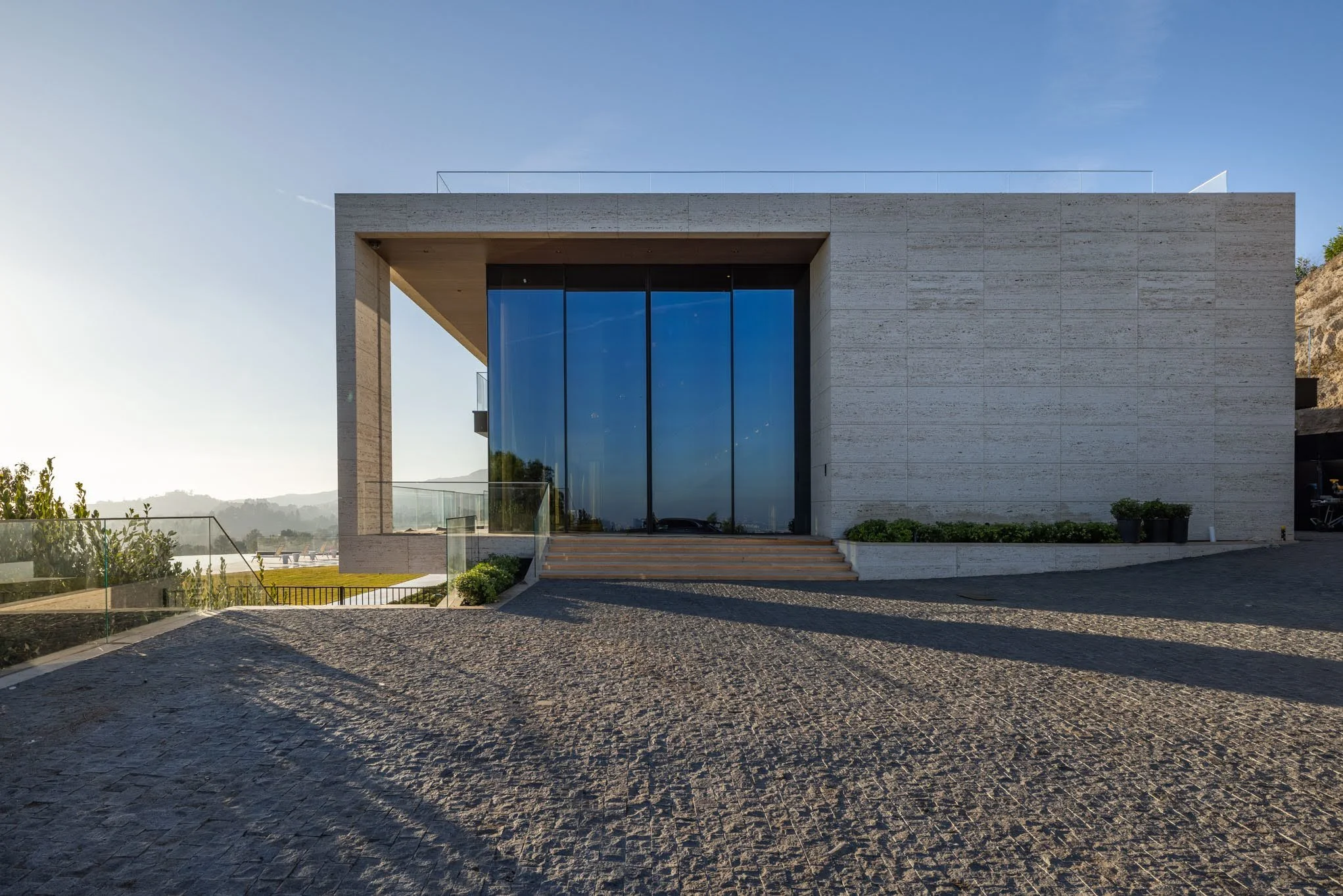 Modern building with large glass front, stone exterior, and steps leading up to the entrance, with outdoor landscaping and a clear sky.