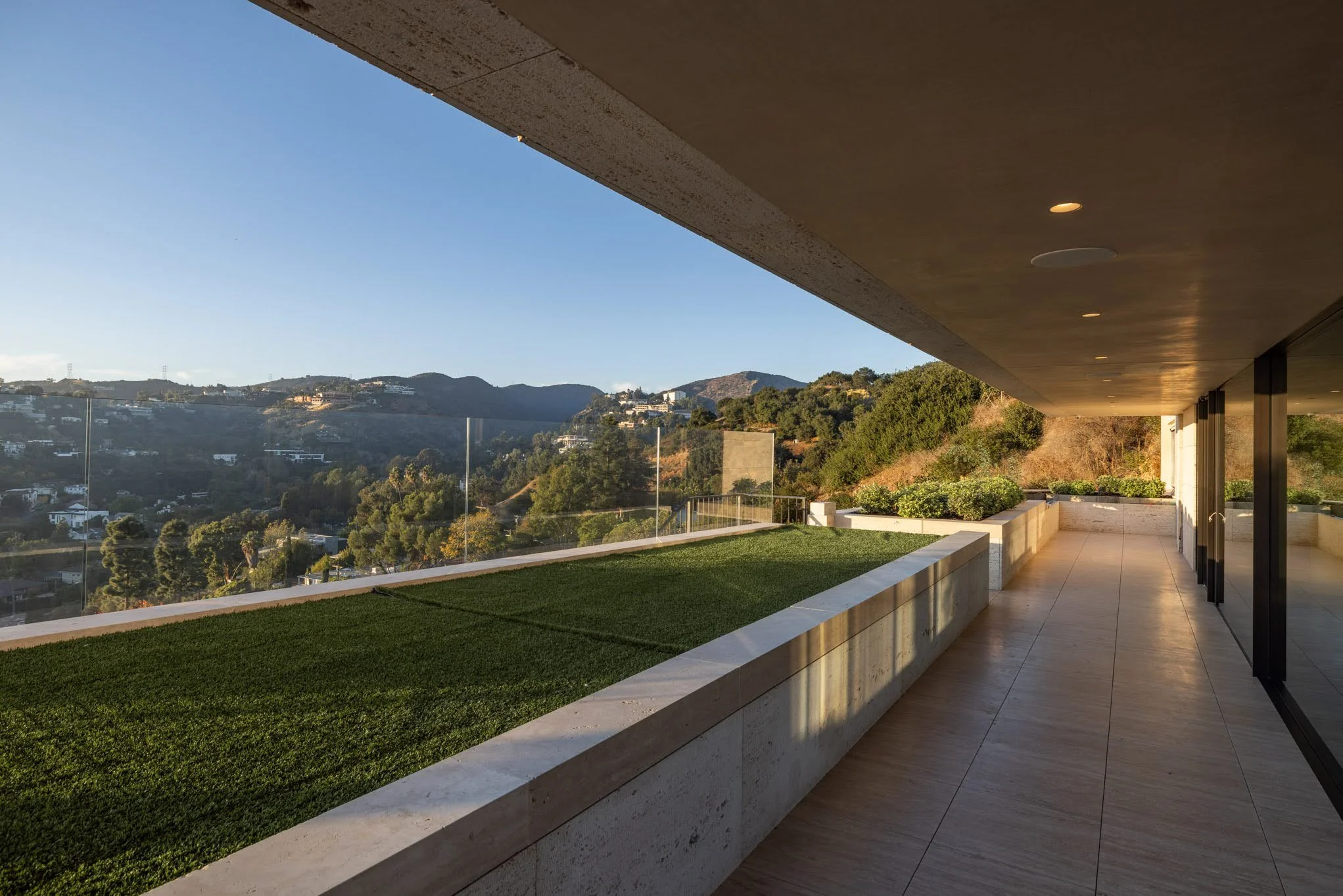 Modern balcony with glass railing overlooking hills and trees at sunset