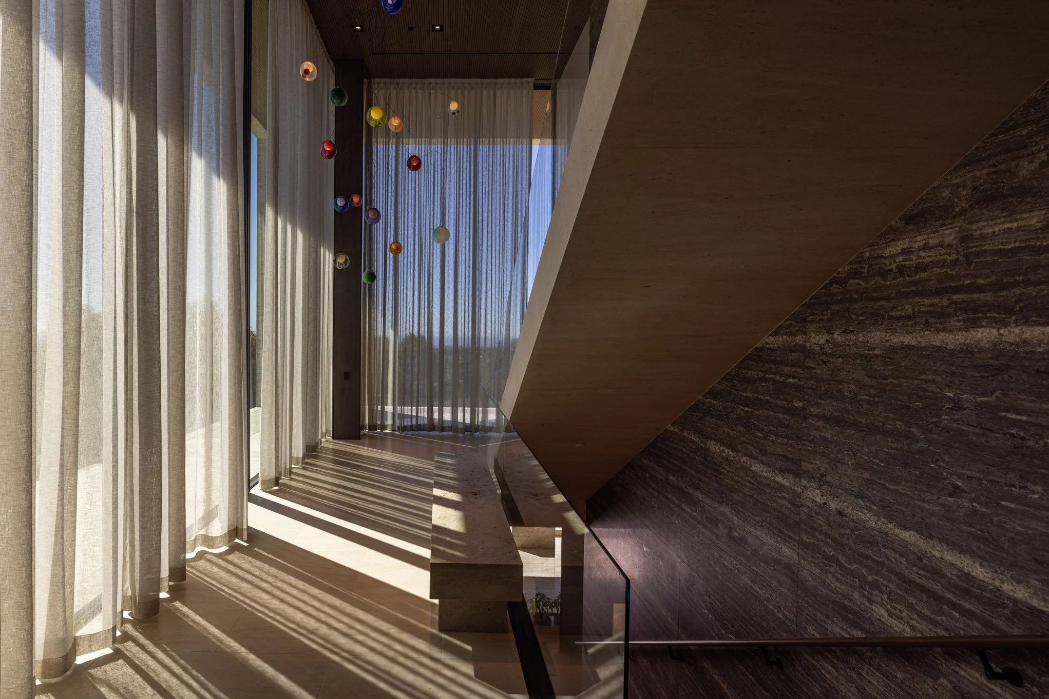 Sunlight streaming through sheer curtains onto a staircase with colorful hanging ornaments