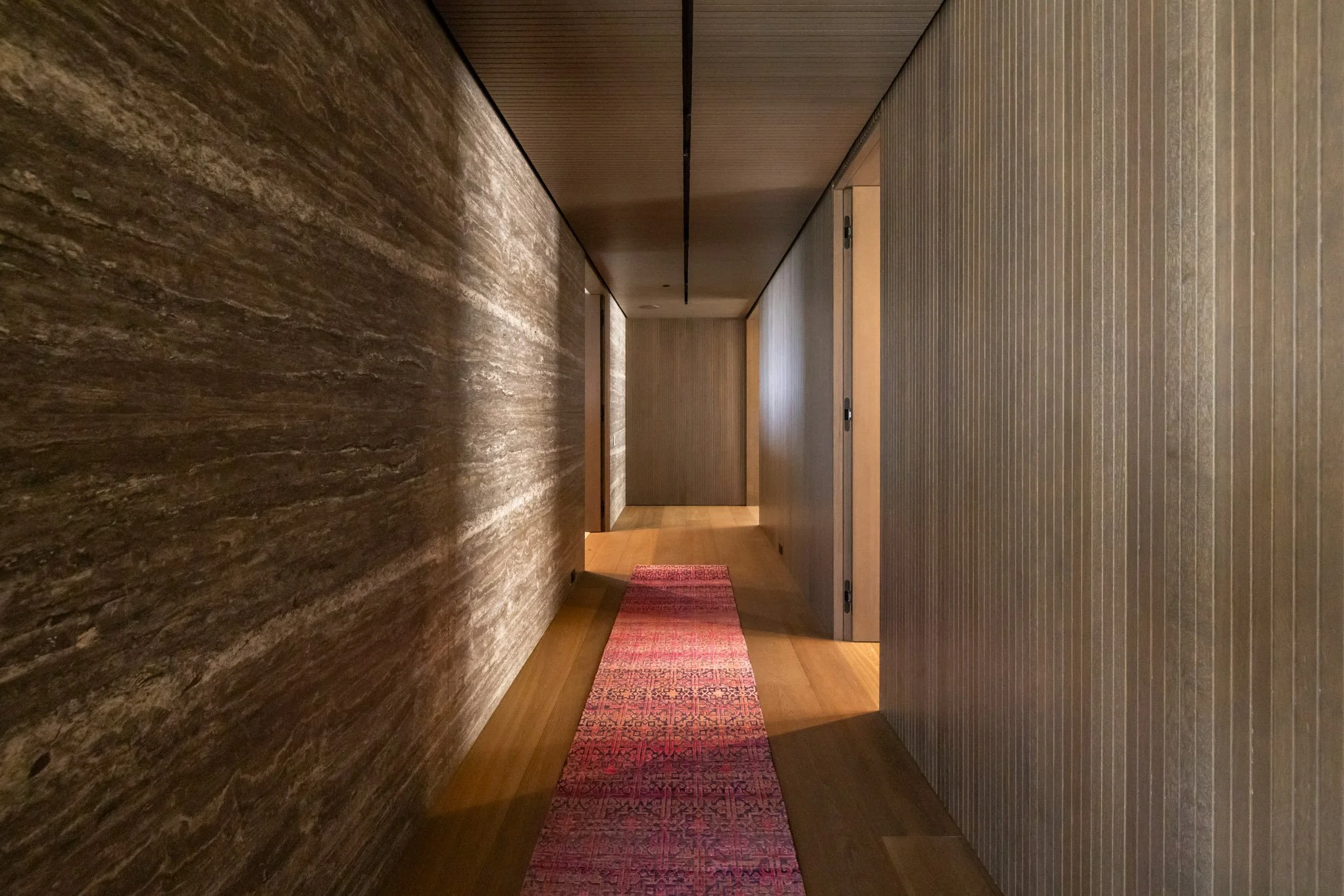 A narrow hallway with textured brown and beige walls, wooden flooring, and a red carpet runner.