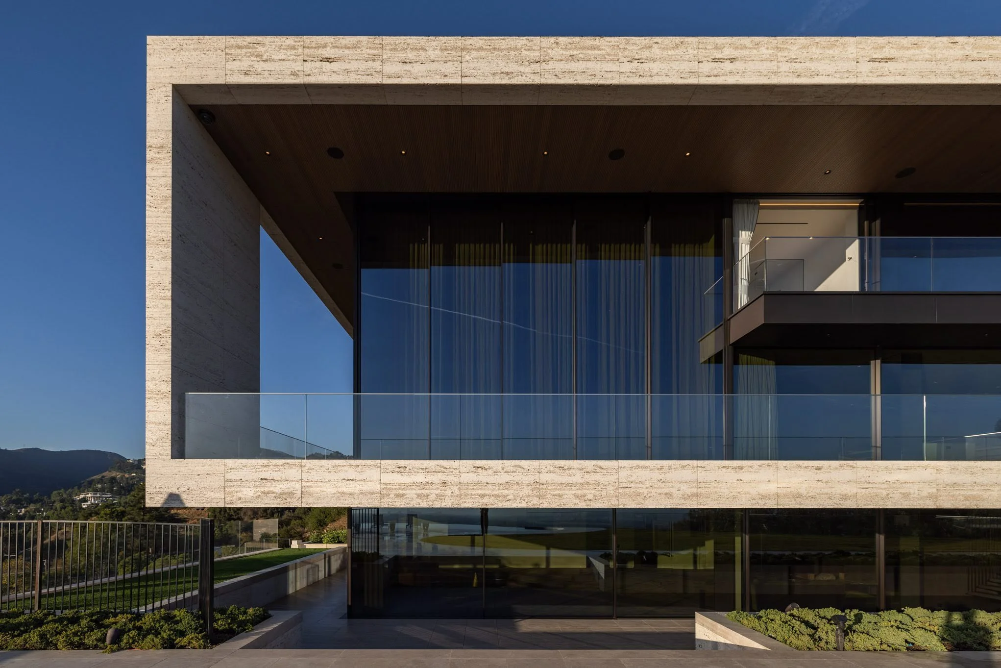 Modern building with large glass windows and balconies, with a mountain and clear blue sky in the background.