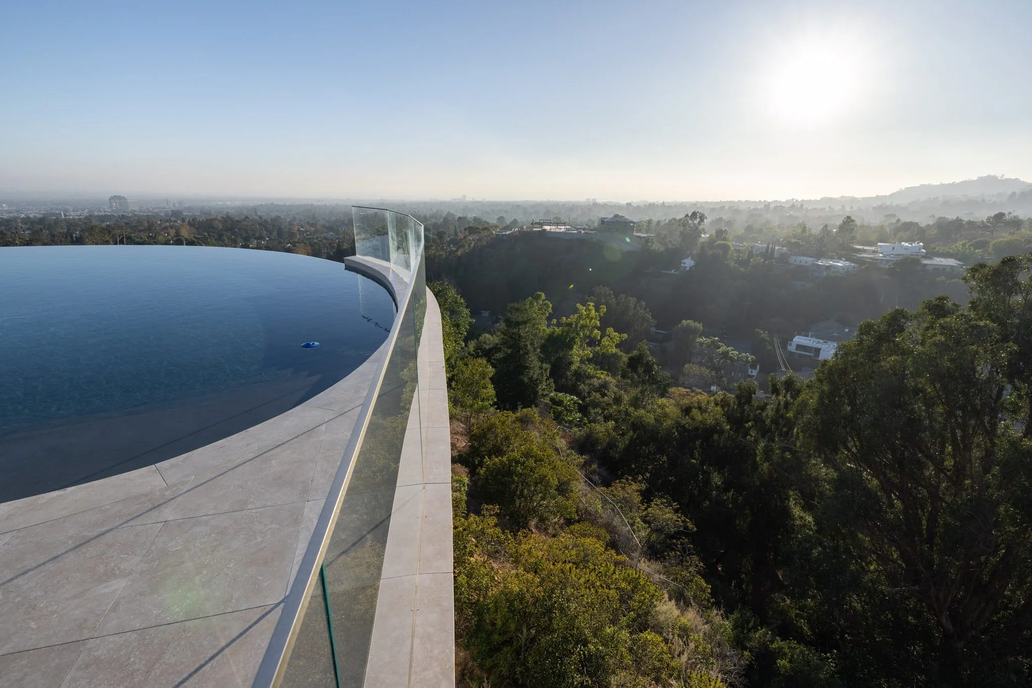 Infinity pool on rooftop overlooking city and greenery at sunset.
