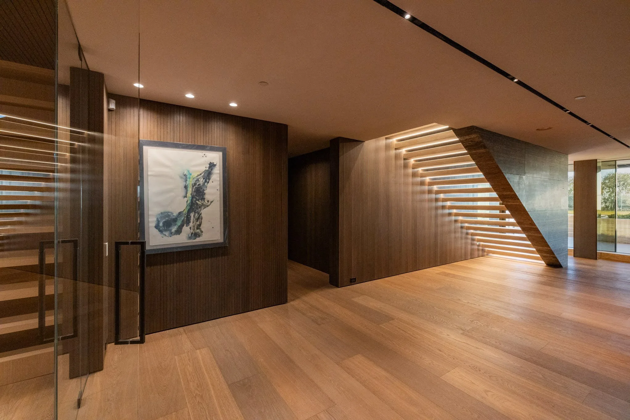 Modern interior space with wooden flooring, a wooden wall with art, and a staircase with horizontal wooden slats